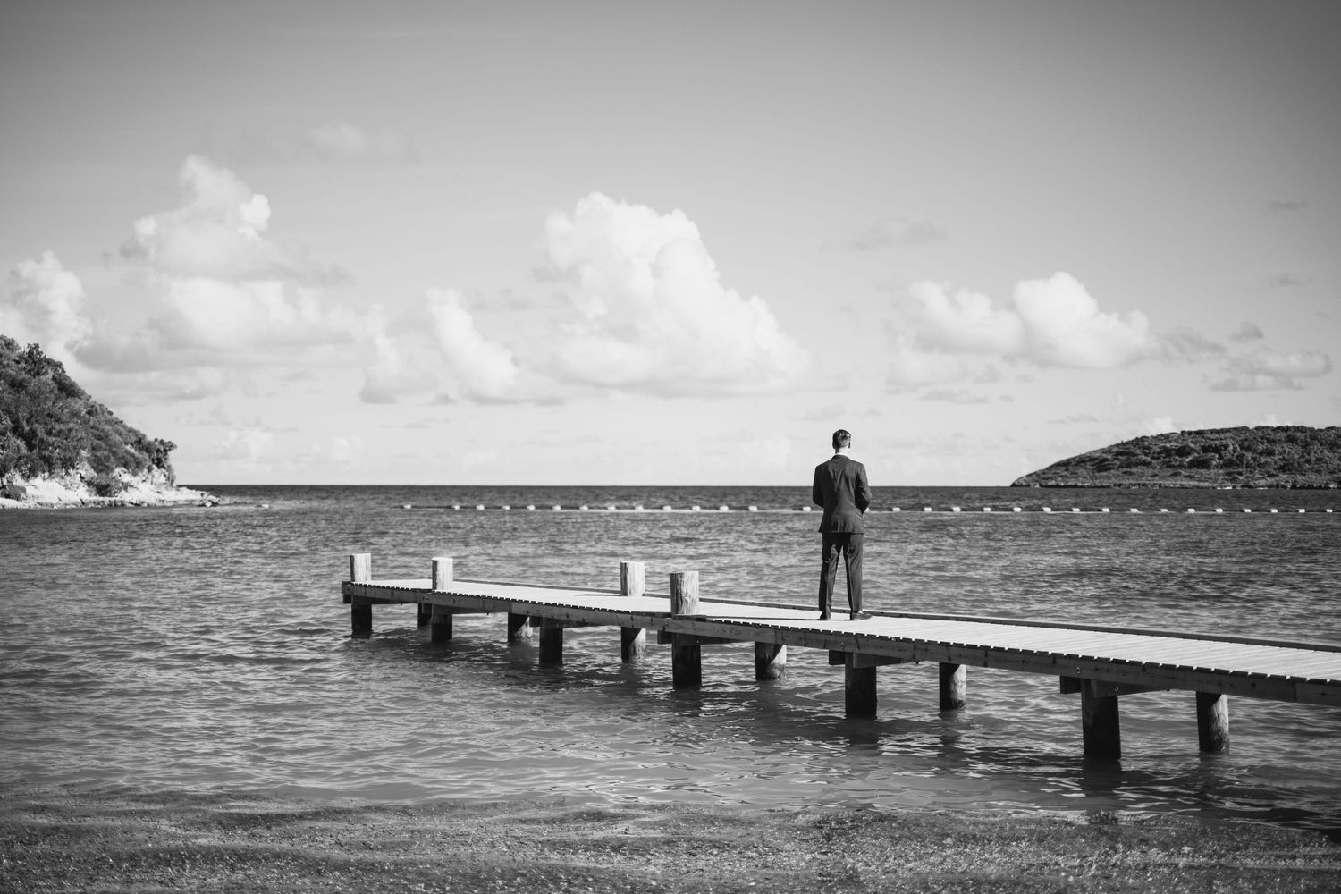 Black and white photo of a solitary figure standing on a wooden pier extending into the ocean.