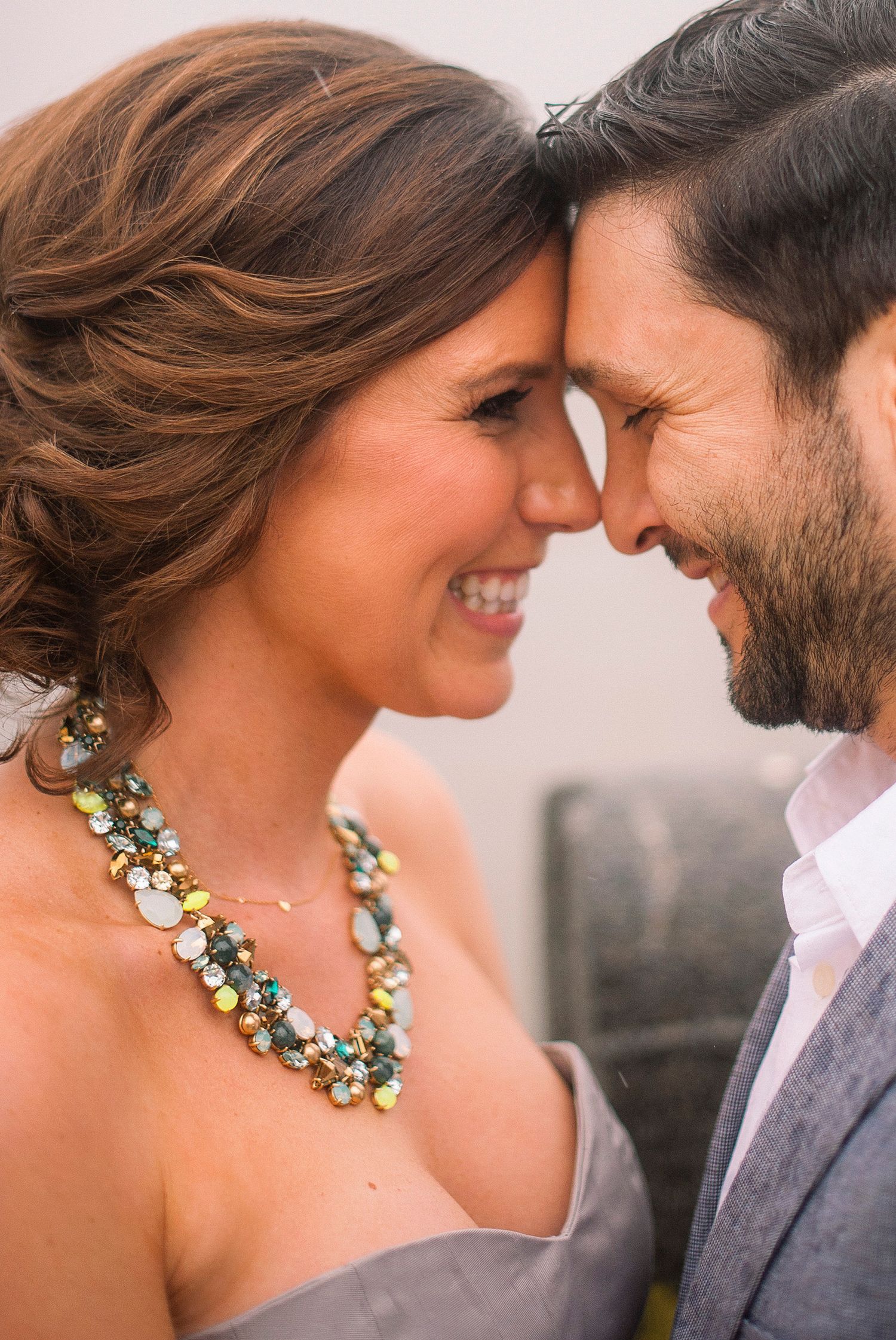 Romantic close-up of couple wearing statement necklace and gray suit.