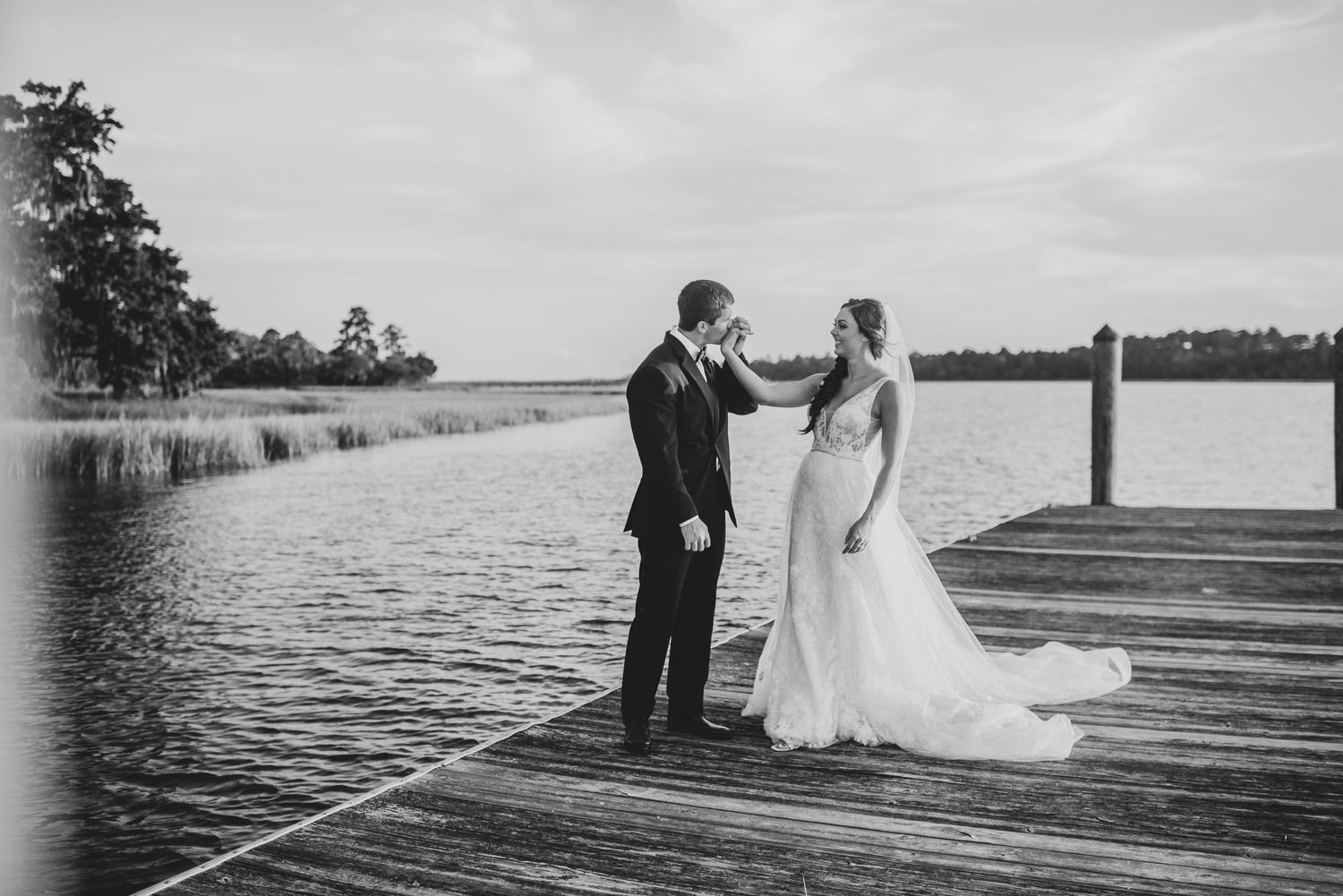 Romantic black and white wedding photos of a couple on a lakeside dock at sunset.