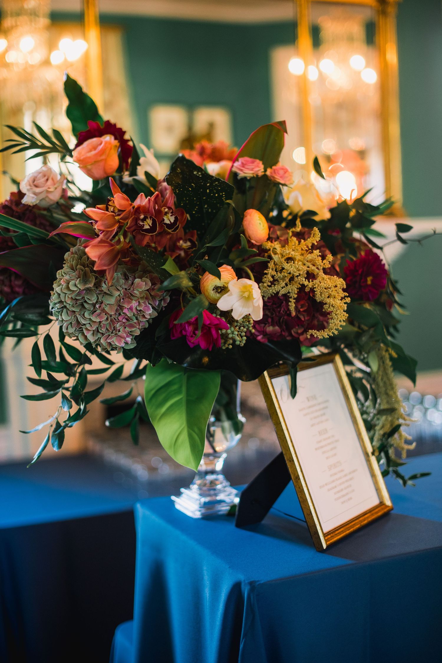 Elegant floral centerpieces with pink and burgundy blooms on royal blue tablecloths with framed menu cards.