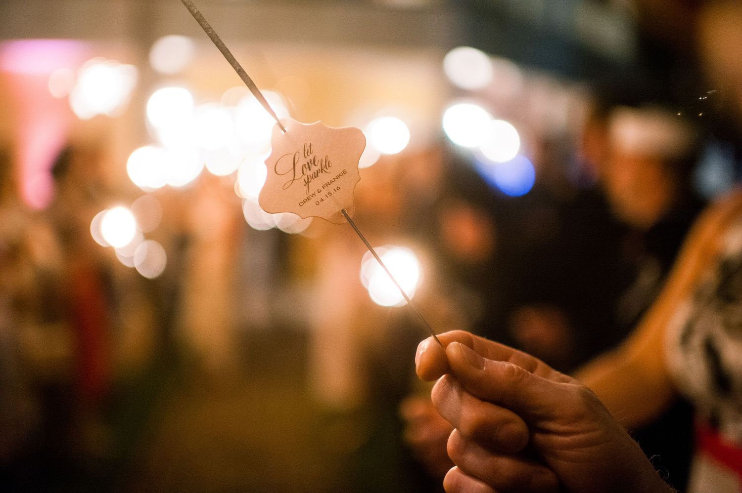 People hold sparklers at night creating a magical bokeh effect with glowing lights in the background.