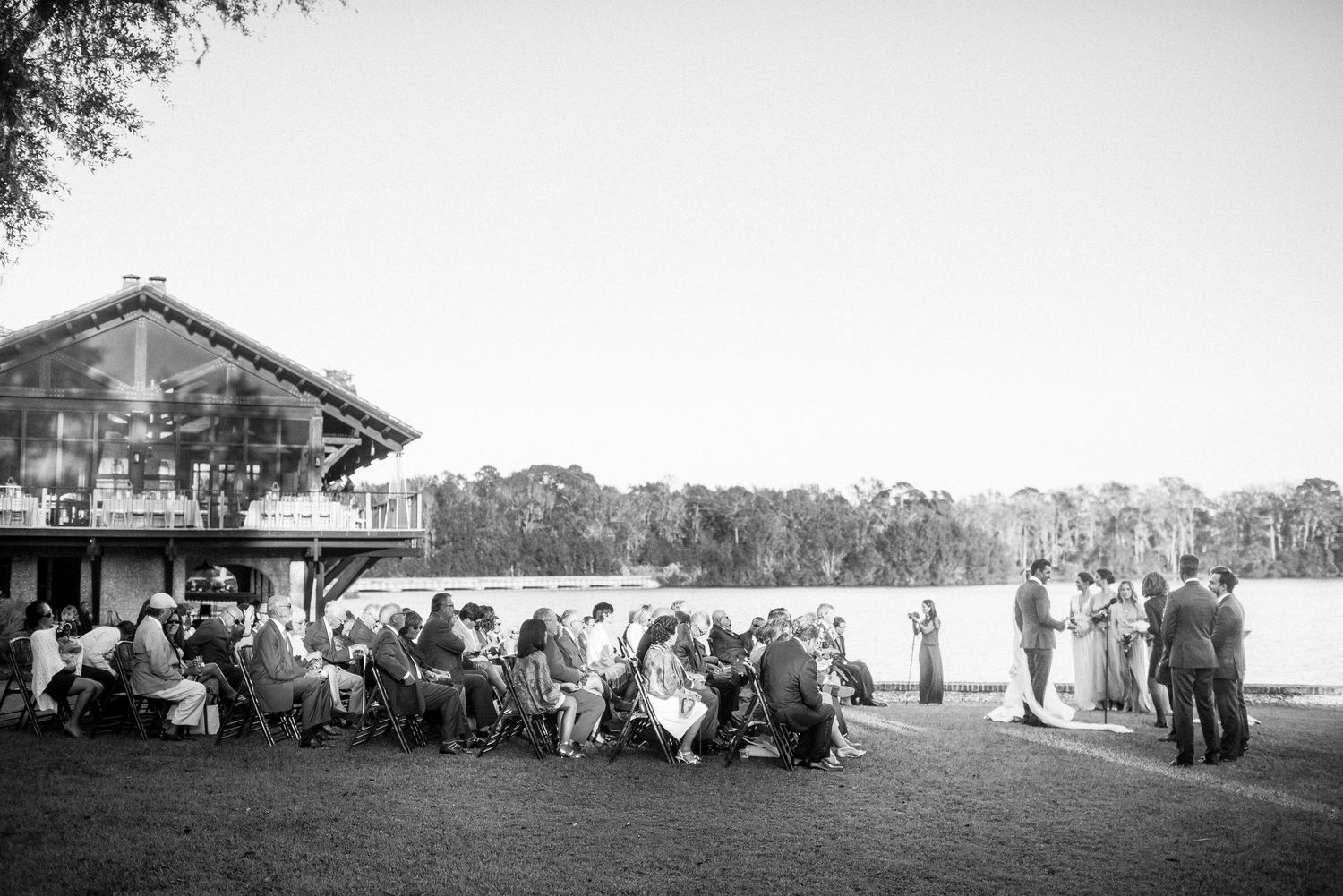 Black and white panoramic view of guests gathering outside a rustic building for an outdoor event.