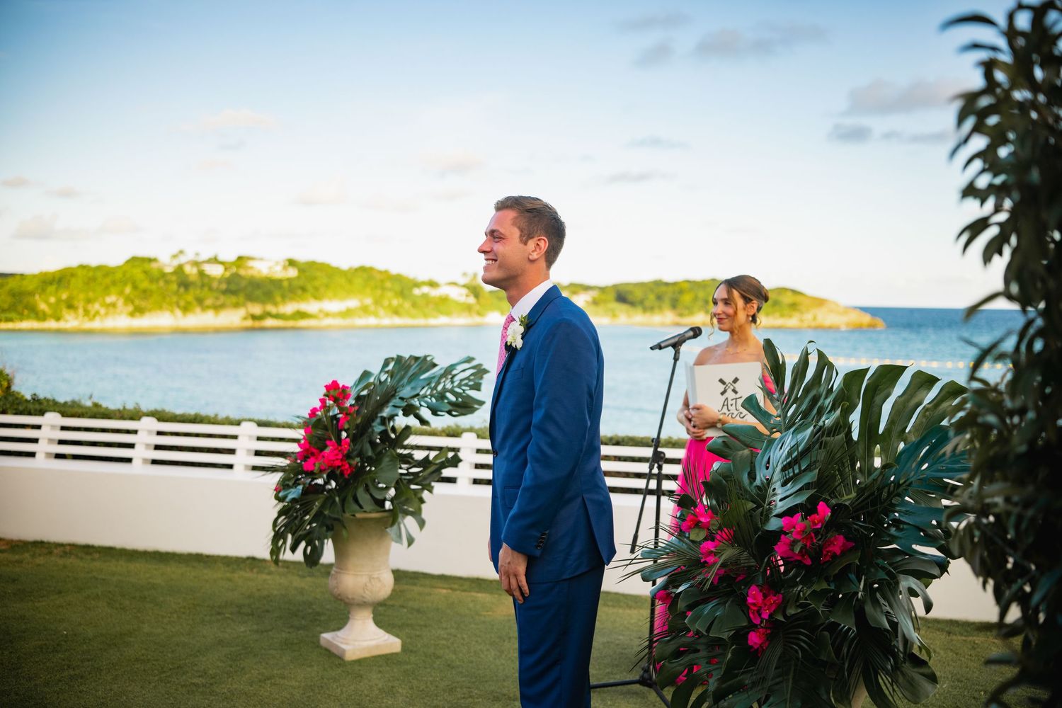 Oceanfront wedding ceremony setup with tropical flowers and white fencing.