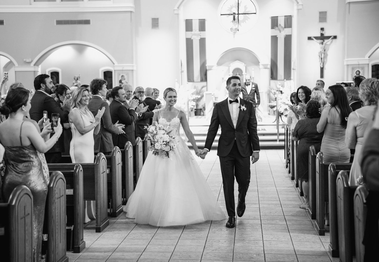 Black and white panoramic shot of wedding ceremony guests seated in church pews.