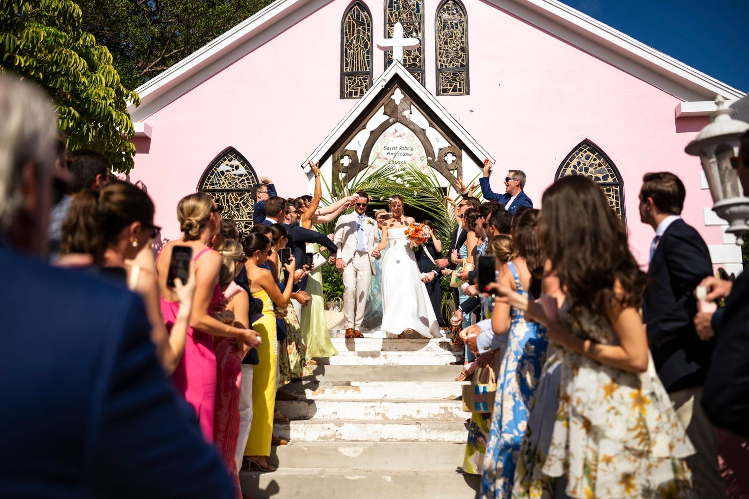 Guests gather outside a charming white chapel with gothic windows as a couple descends the stairs after their ceremony.