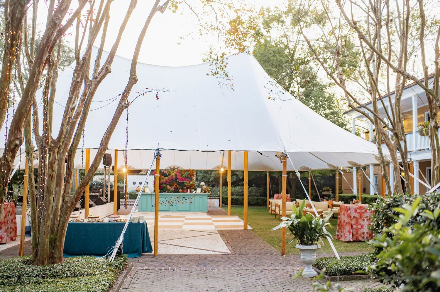 A series of white wedding tents set up outdoors along a tree-lined path with ocean views in the background.