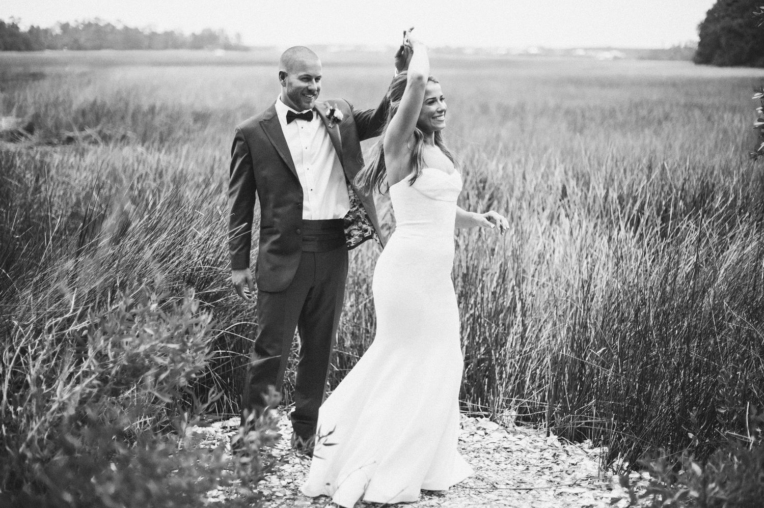 A romantic black and white photo series of a couple embracing in a serene meadow during a wedding celebration.