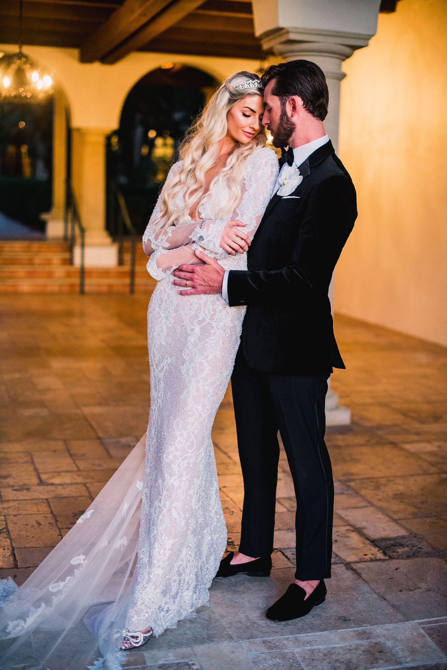 Newlyweds share tender moments on stone tiles with warm lighting and elegant wedding attire.