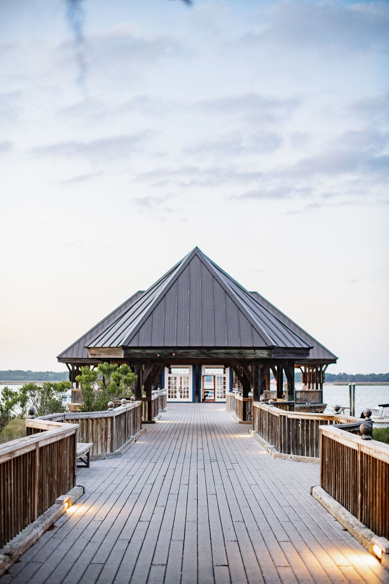 A series of wooden pier boardwalks with covered pavilions extending over a calm lake under cloudy skies.