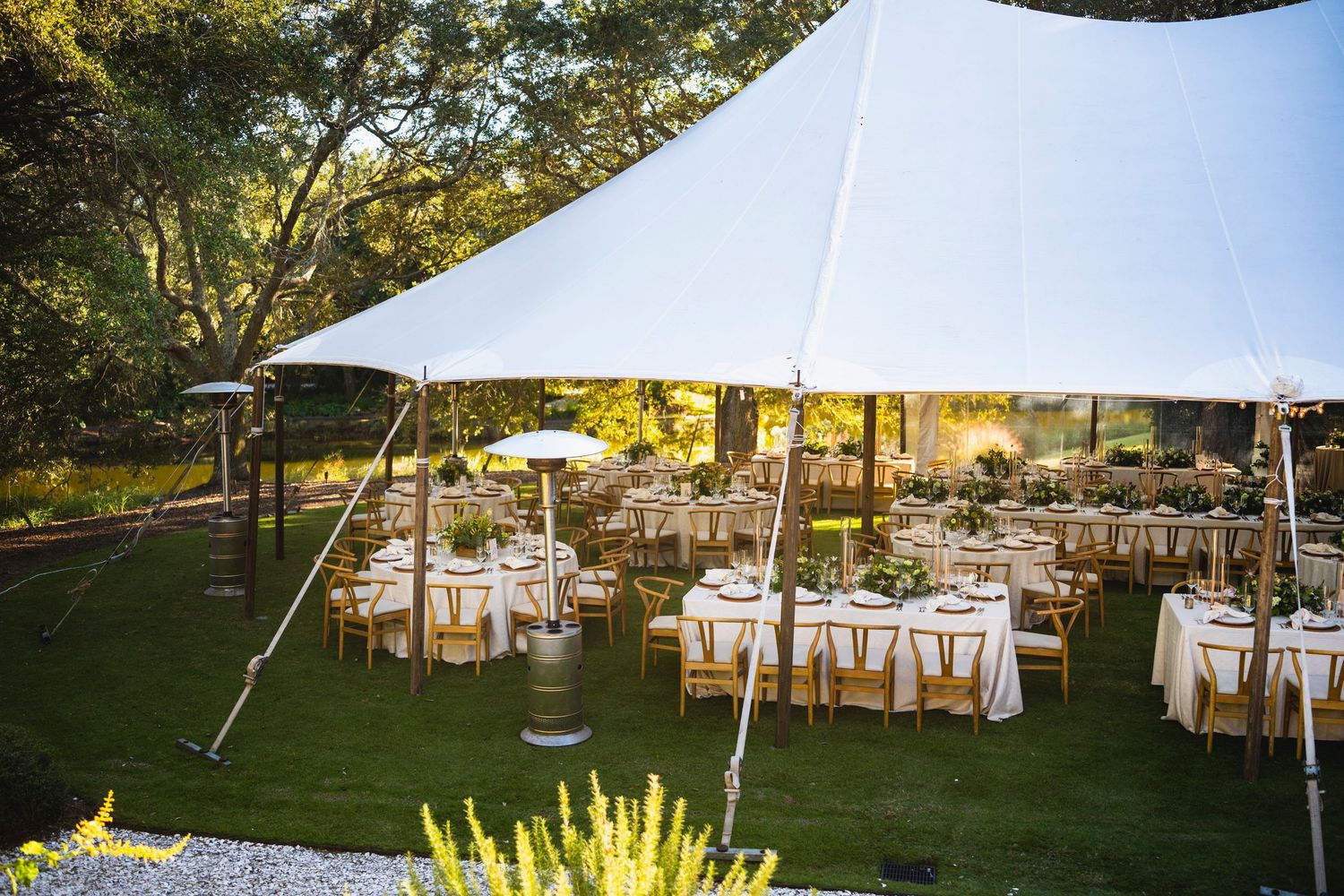 White wedding reception tables and chairs set up outdoors under trees with string lights creating a romantic garden atmosphere.