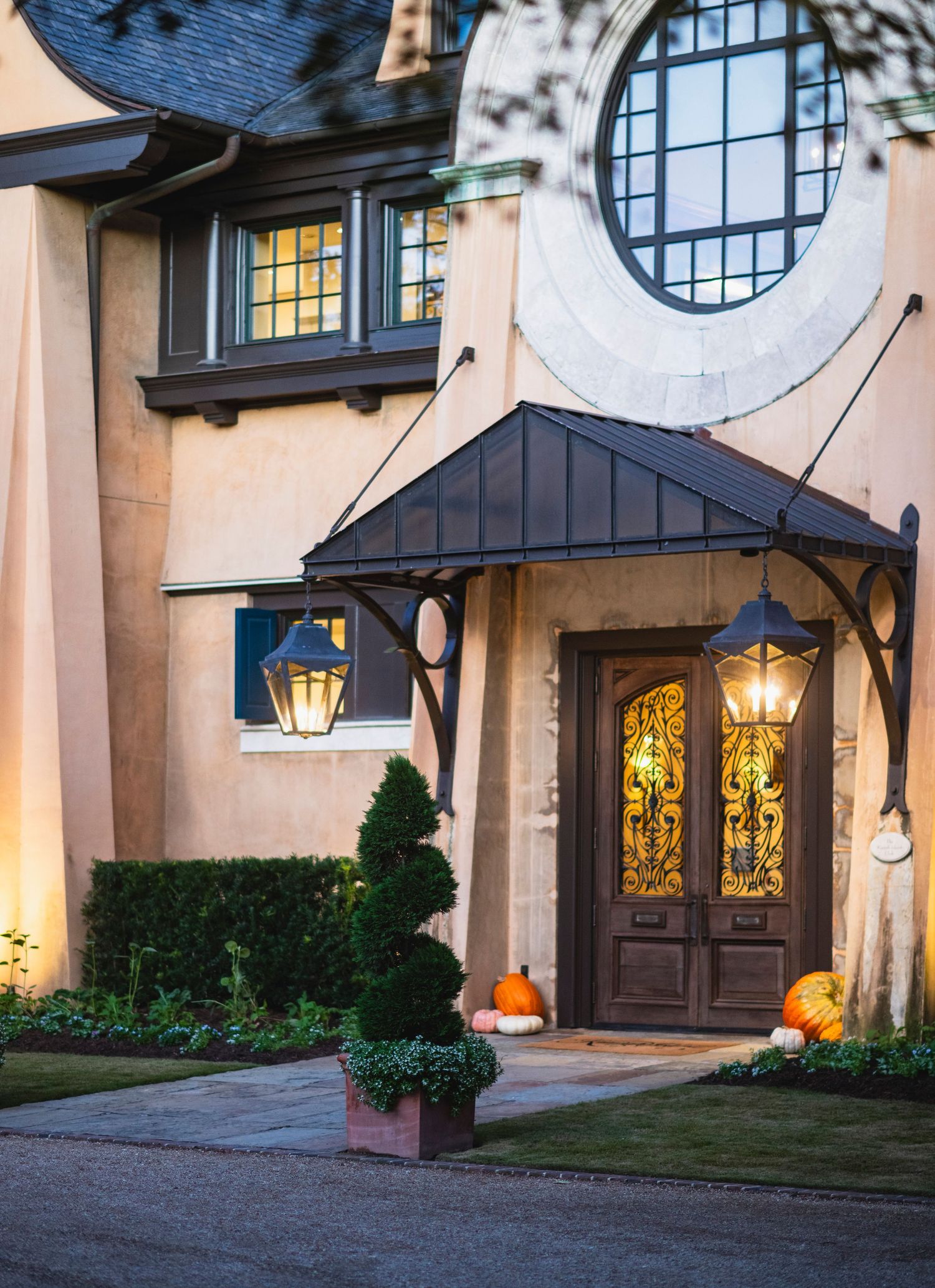 A series of decorative pumpkins arranged on a doorstep with glowing windows and circular architectural details at dusk.