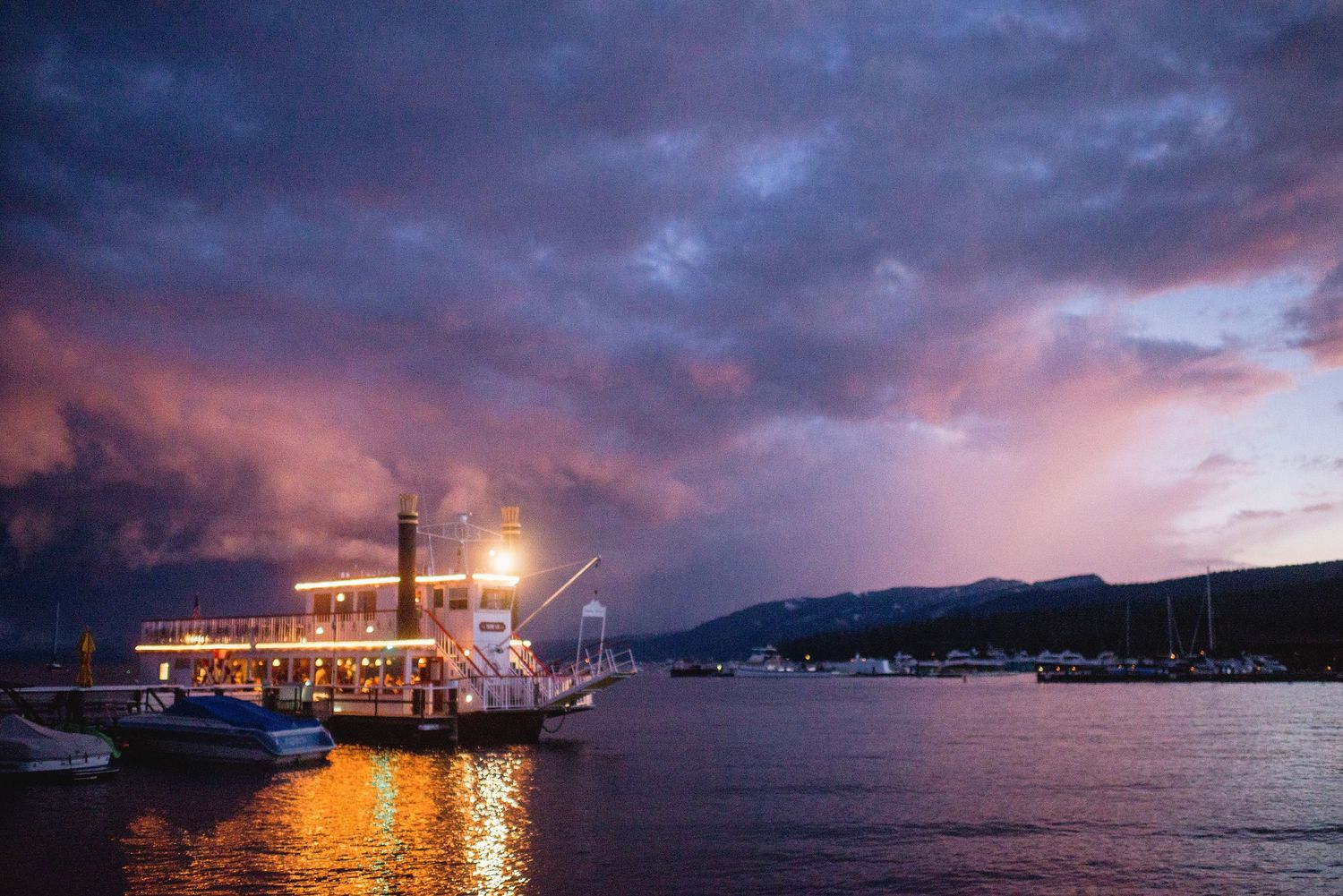 Twilight harbor panorama in Lake Tahoe, CA with glowing lights reflecting on calm waters against purple sky.