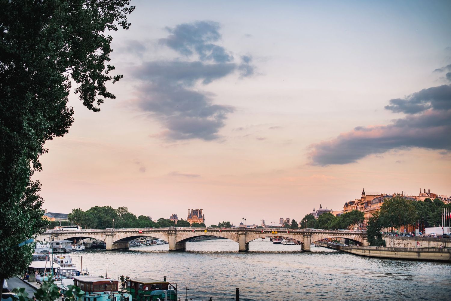 Scenic sunset view of the Seine River and bridges in Paris with soft pink and purple sky.