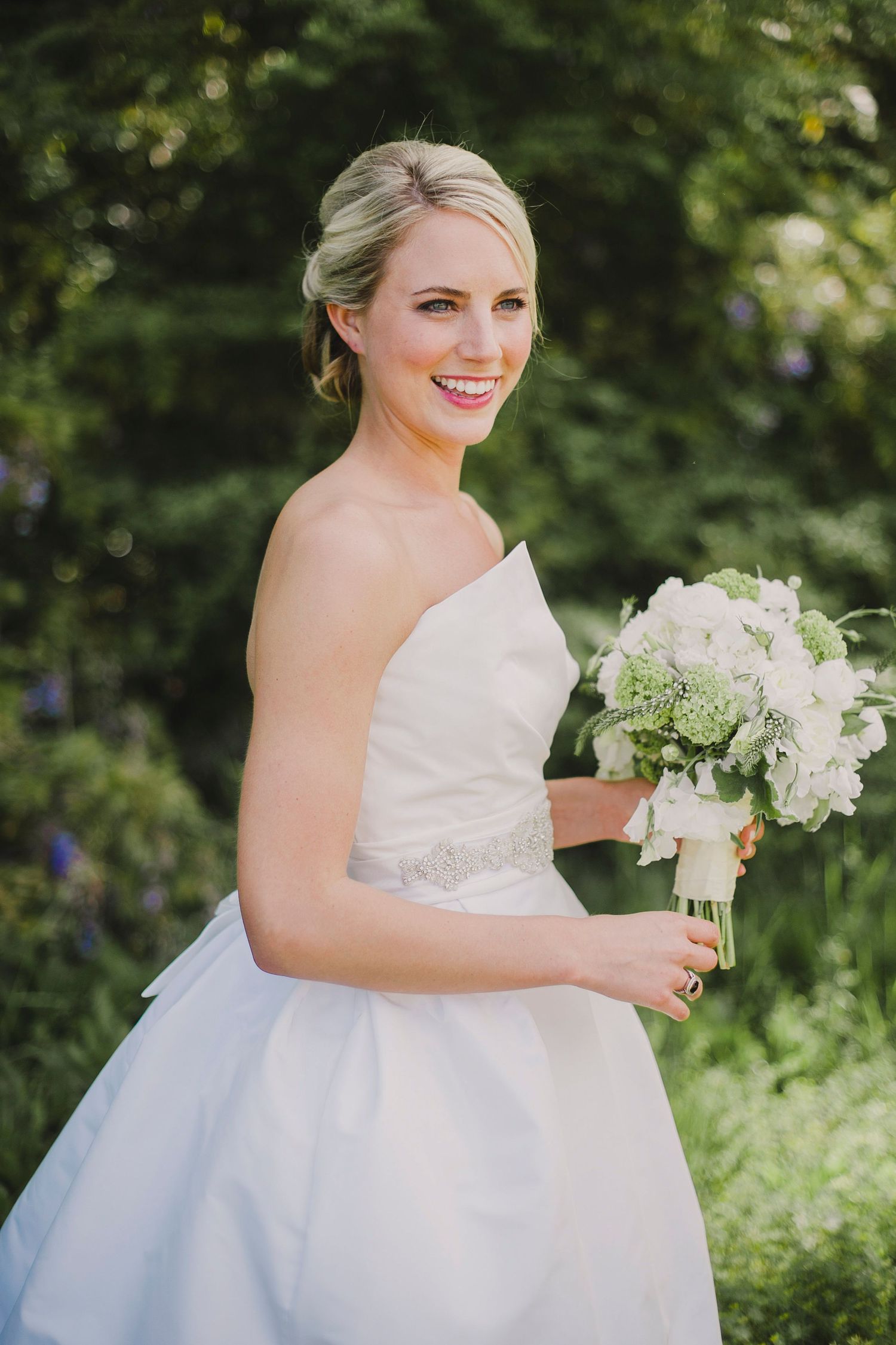 Bride in white dress holding bouquet of flowers in garden setting.