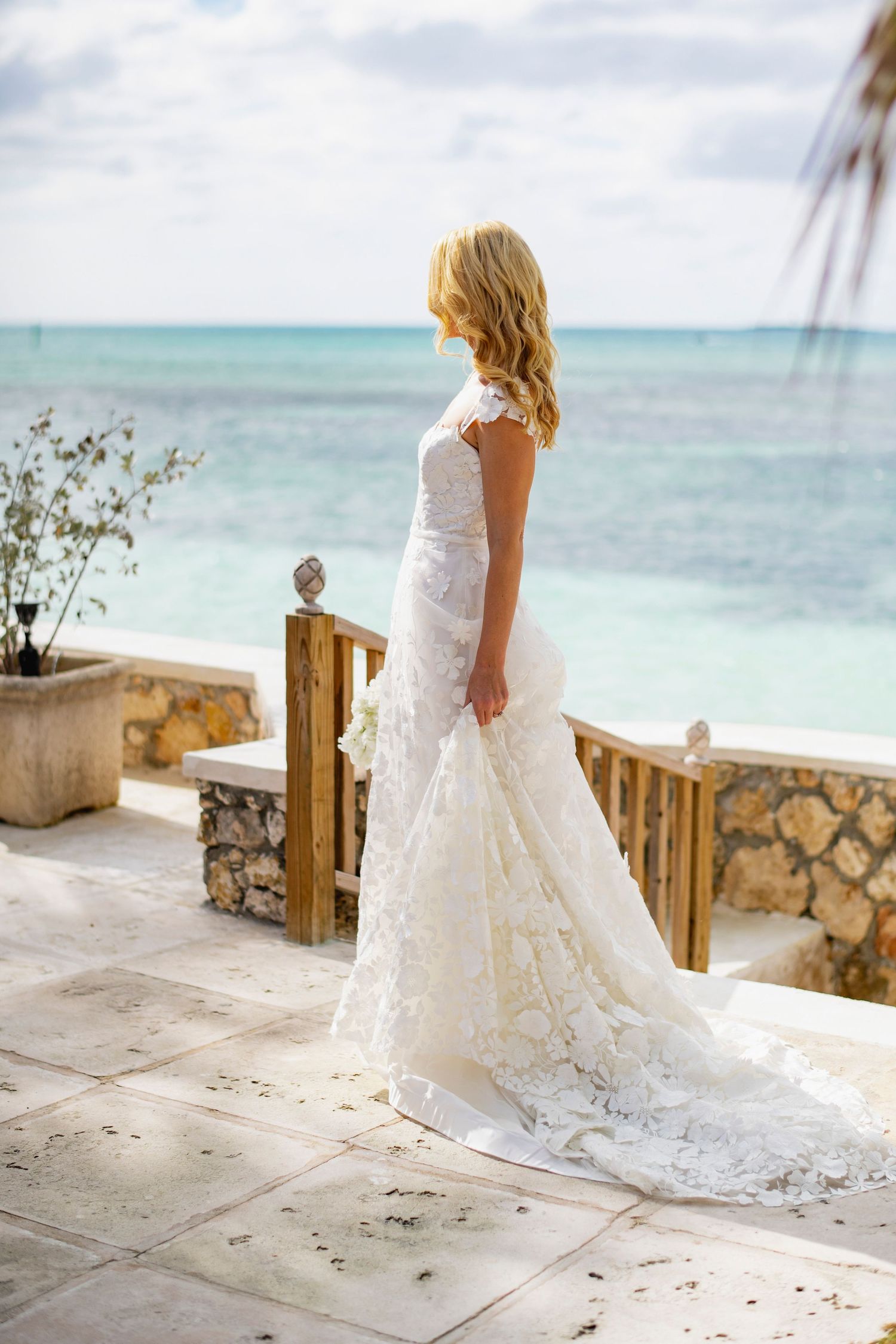 White wedding dress flowing in the breeze against a tropical beach backdrop with turquoise waters.