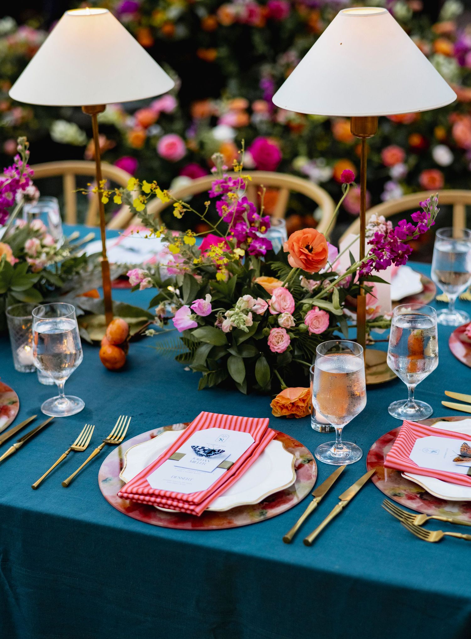 Elegant table setting with navy linens, red napkins, and colorful floral centerpieces.