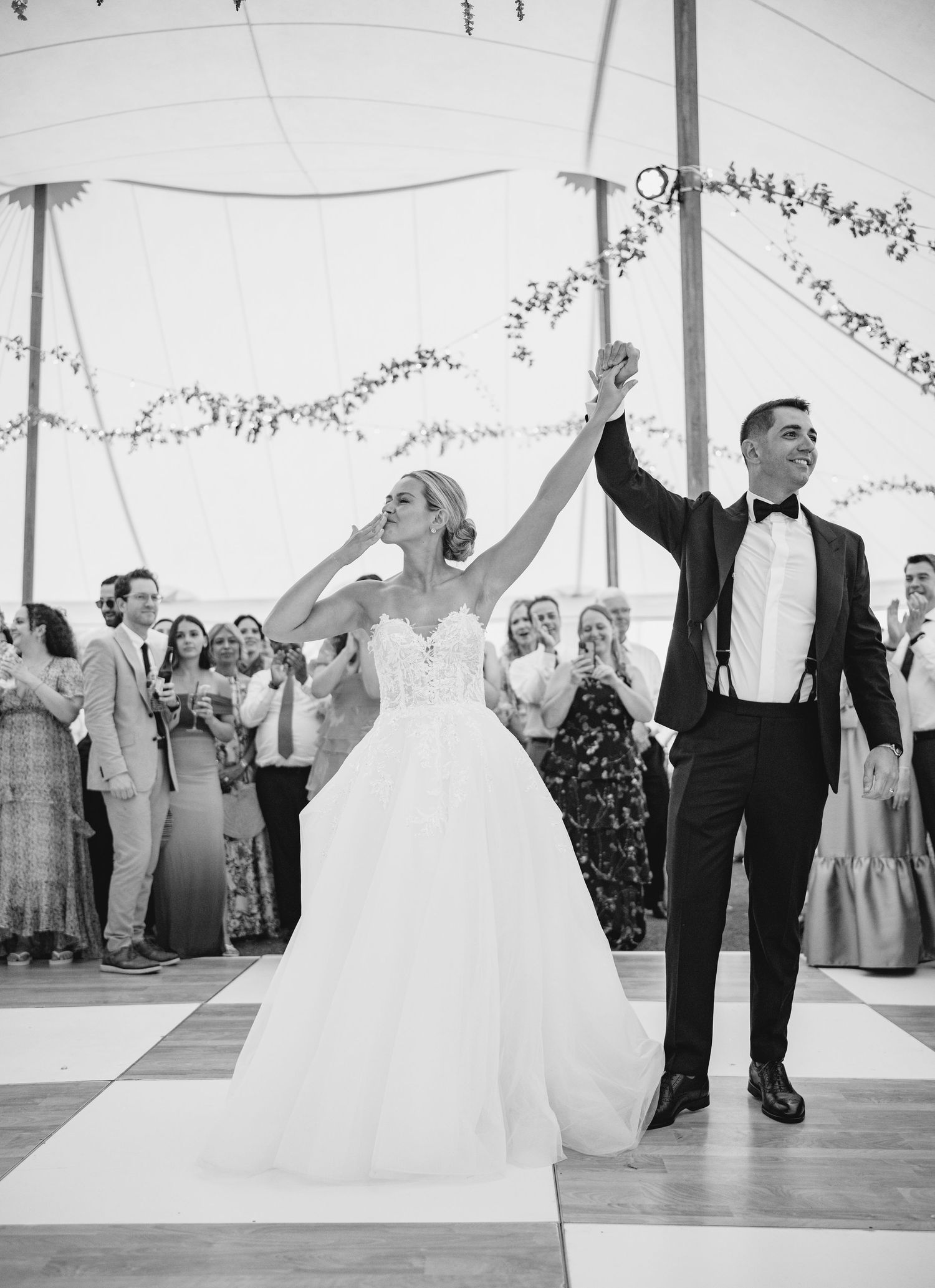 Wedding celebration in white tent with guests dancing and raising hands in celebration.