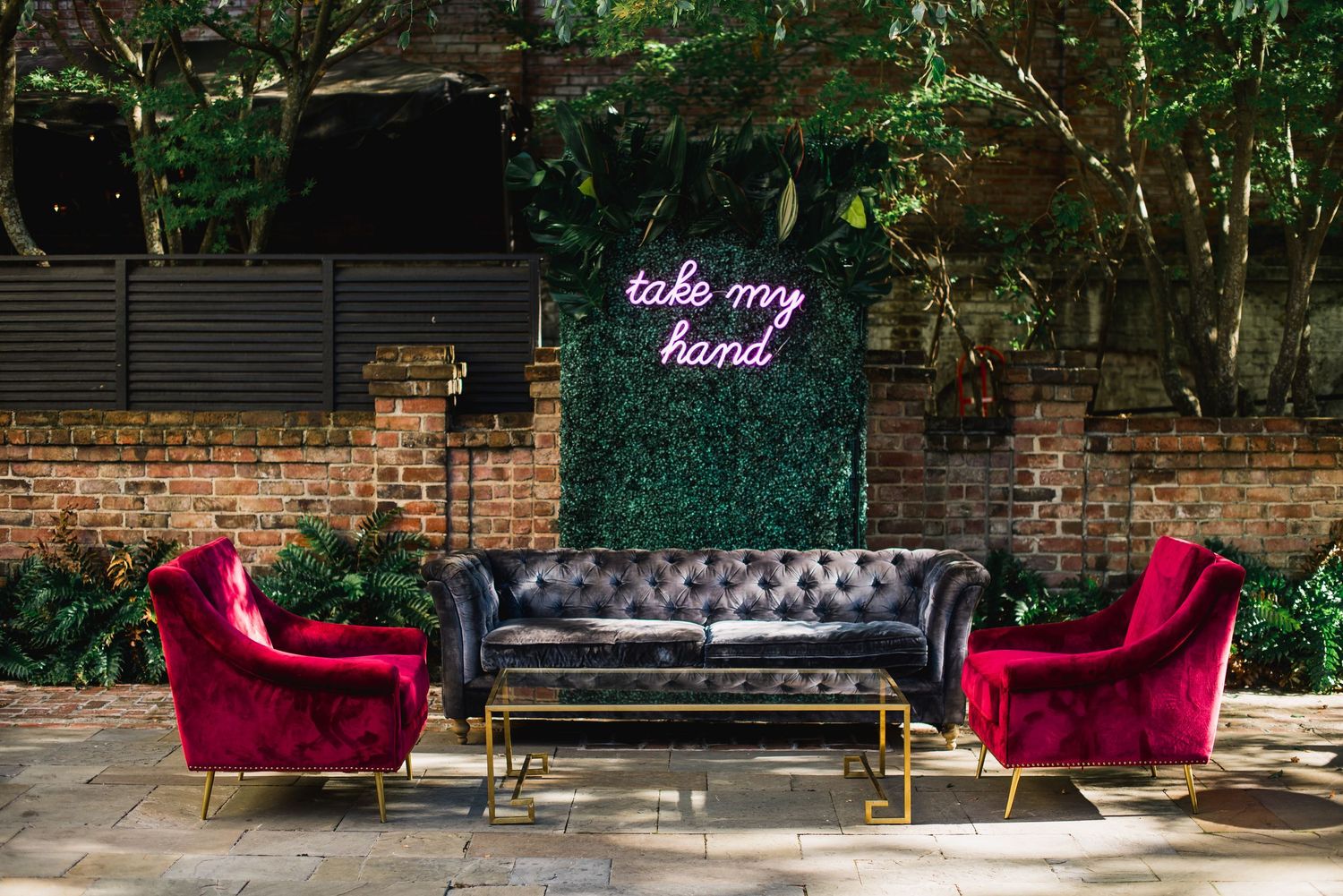 A stylish outdoor seating area features a black leather tufted sofa and burgundy velvet accent chairs on a patio.