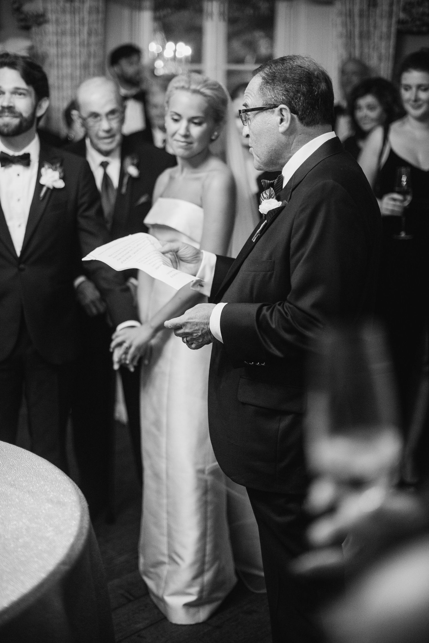 A couple shares their first dance at a wedding reception in black and white with guests looking on.