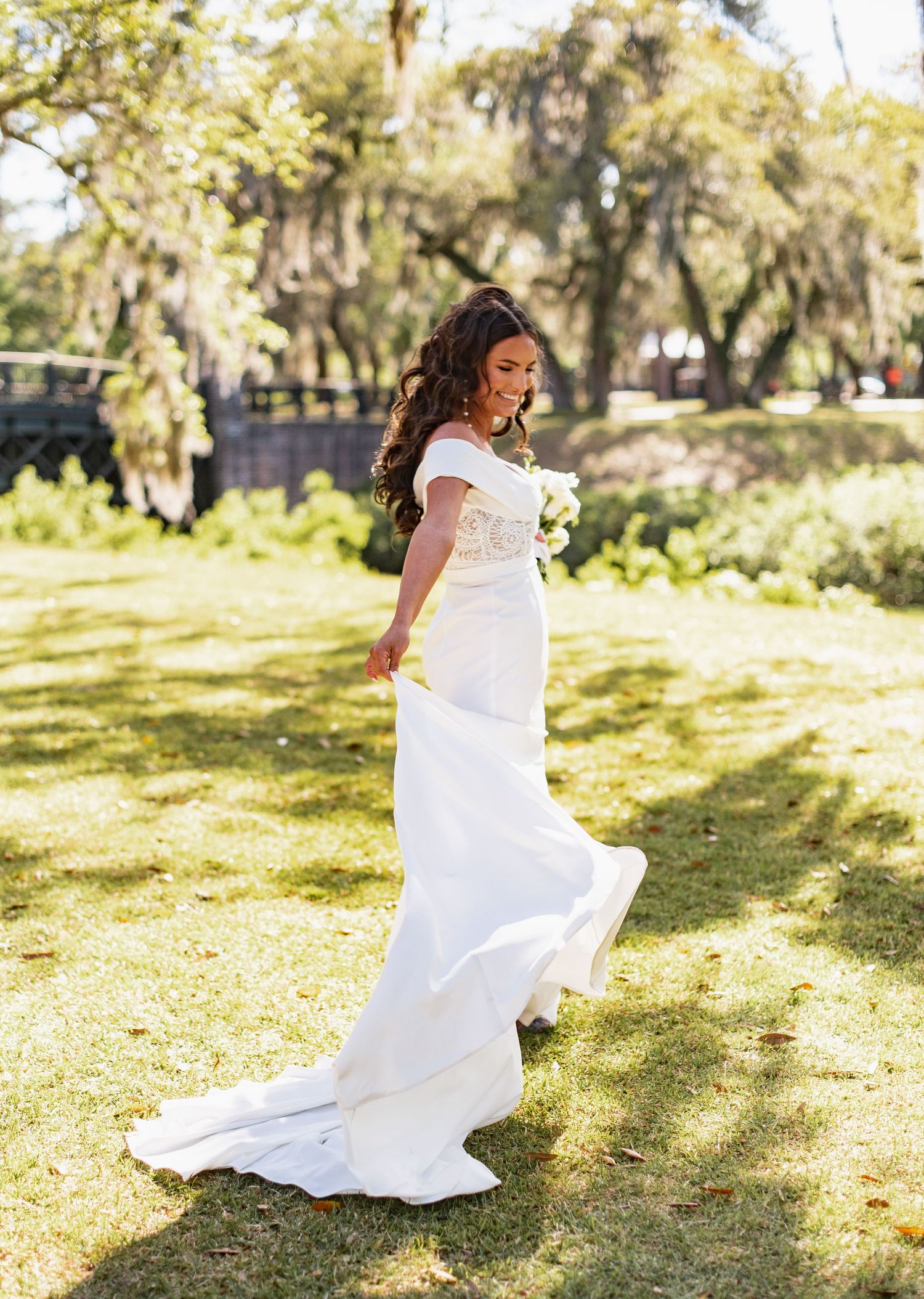 A person in a flowing white dress twirls gracefully in a sunlit garden setting with trees in the background.