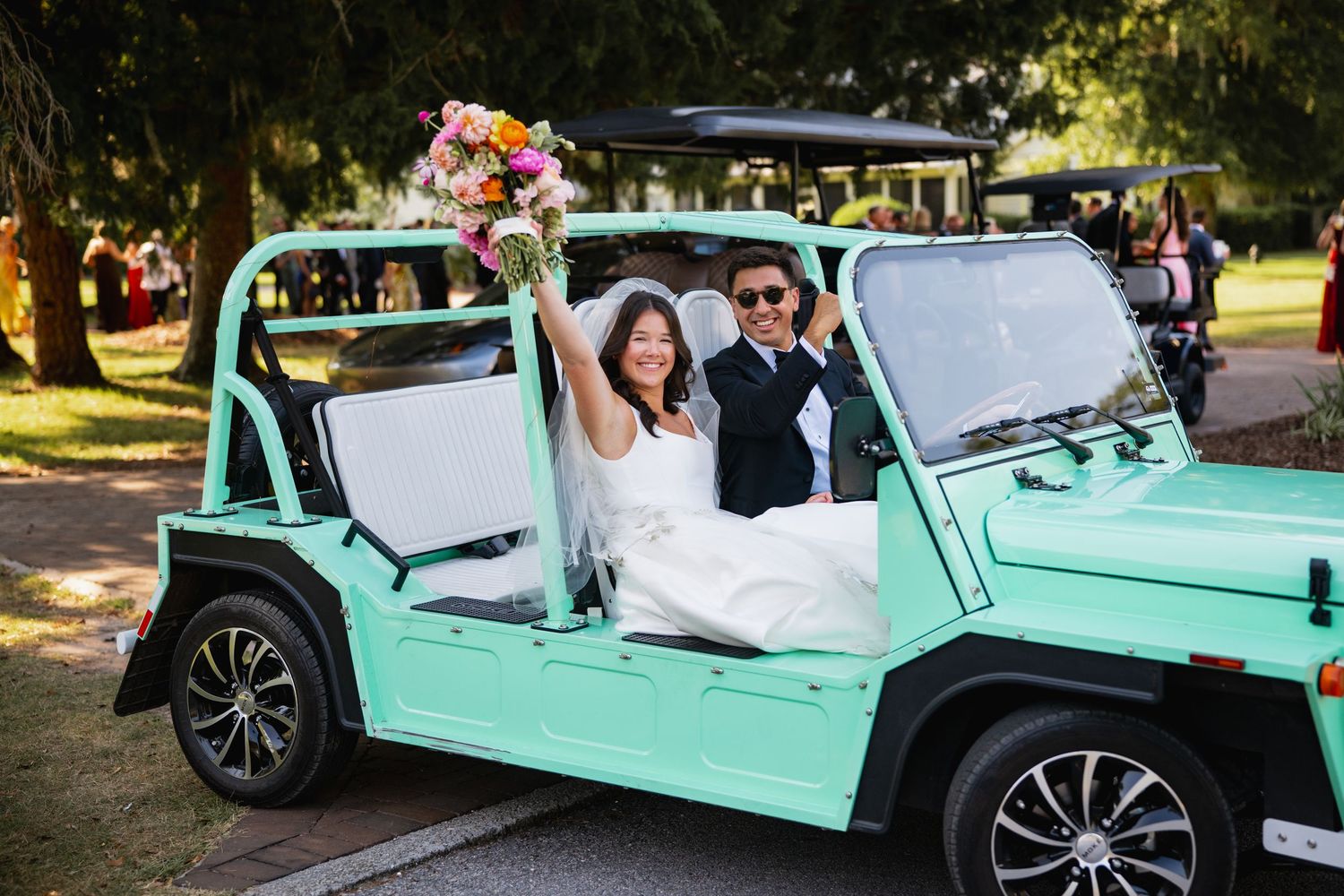 A mint green classic car serves as a wedding getaway vehicle decorated with floral arrangements and ribbons.