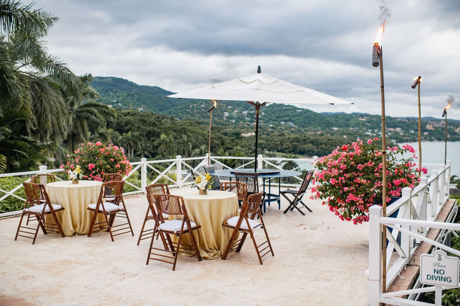 Panoramic view of a beachfront wedding setup with white chairs and floral decorations overlooking a tropical bay.