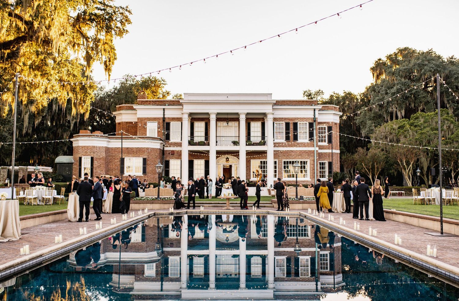 Elegant outdoor swimming pool surrounded by classical architecture and Spanish moss draped trees at sunset.