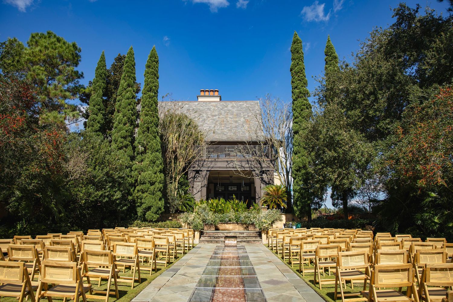 Outdoor wedding ceremony setup with rows of wooden chairs facing a stone altar under bright blue skies.