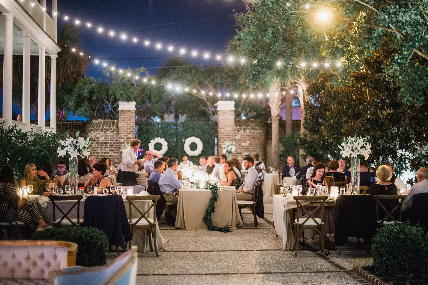 String lights illuminate an outdoor evening wedding reception with guests seated at tables under a starlit sky.