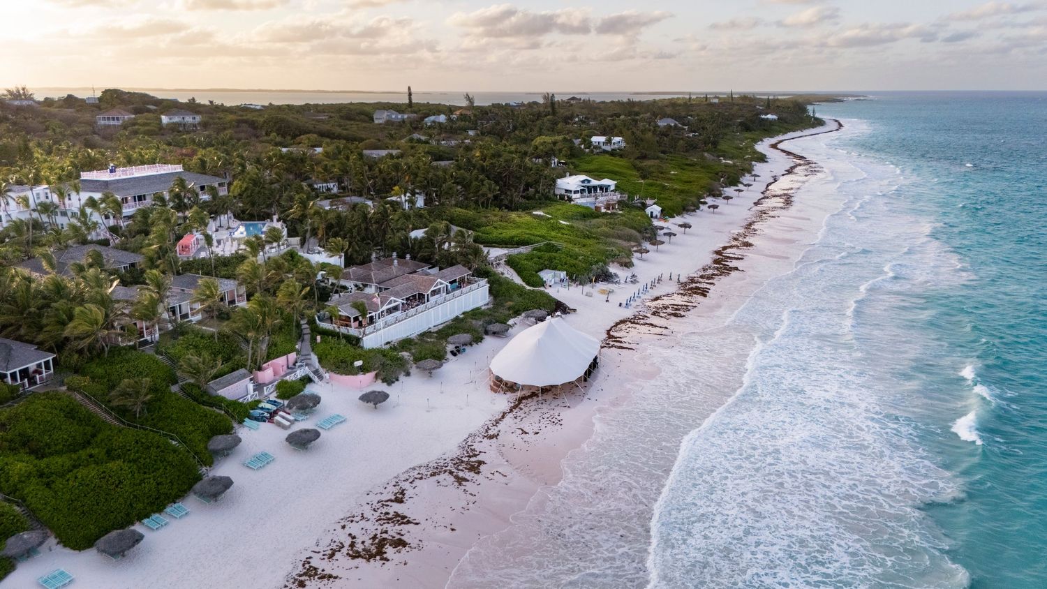 Aerial view of beachfront homes along a pristine coastline with turquoise waters and white sandy beach in the tropics.