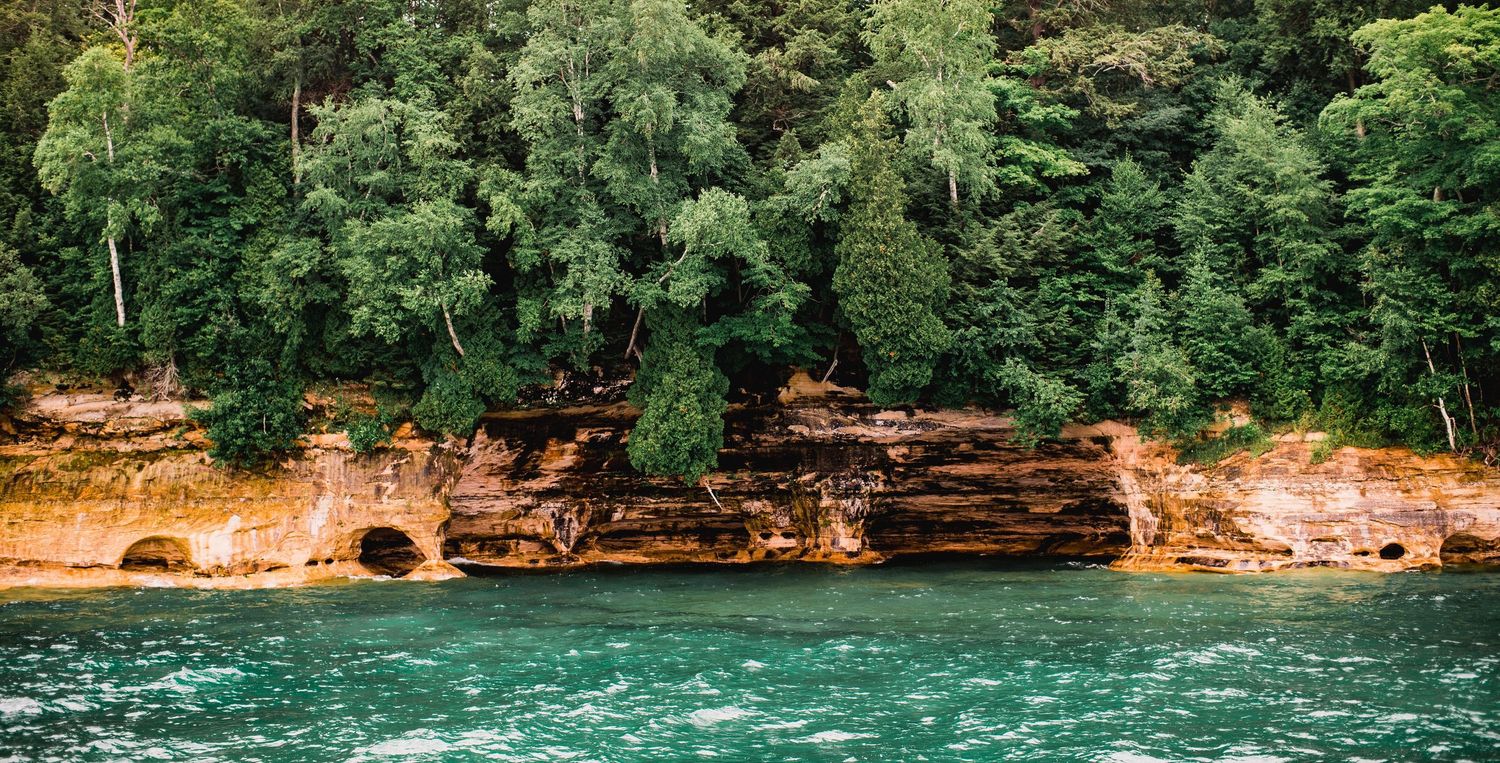 Red sandstone cliffs and dense forest meet turquoise waters along a rugged shoreline.