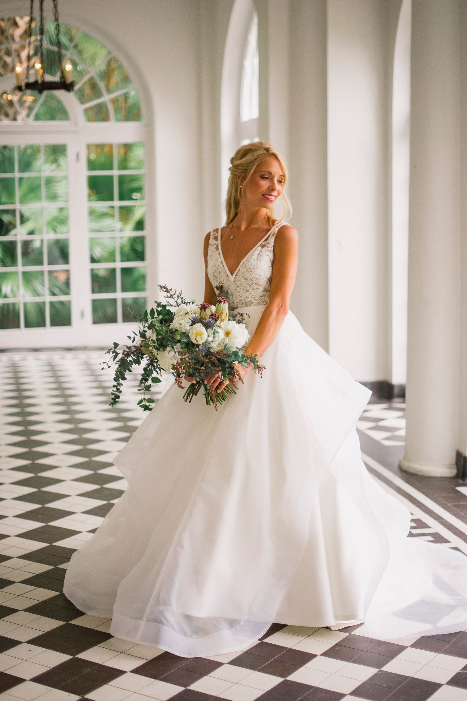 Bride in classic white gown poses on black and white checkered floor in elegant venue.