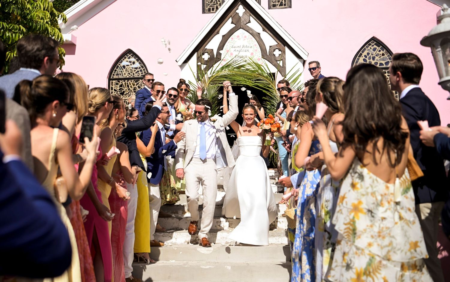 Large crowd gathered outside a pink church for a wedding celebration.