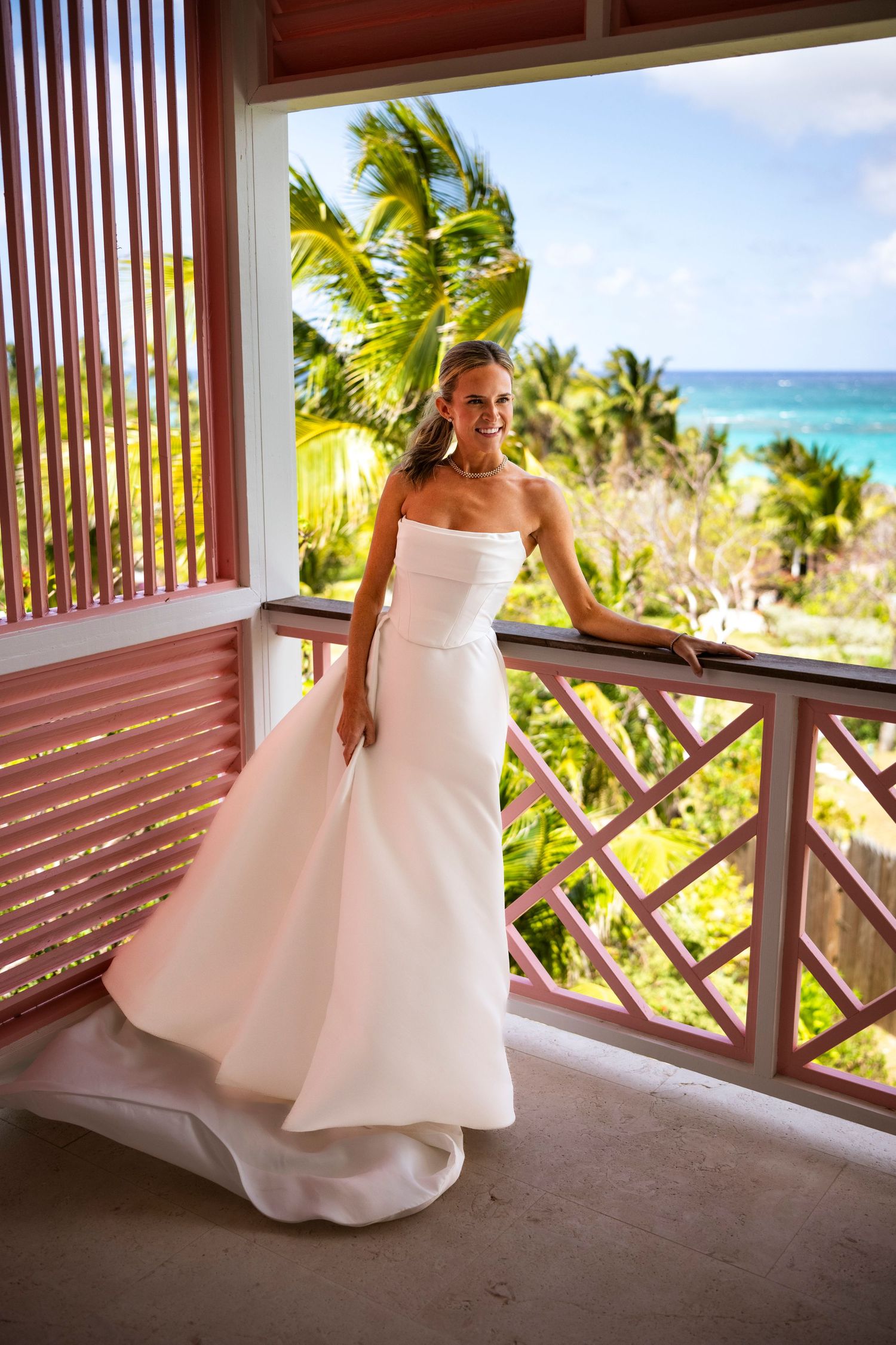 White wedding dress photographed on a tropical beach resort balcony with palm trees and ocean views.