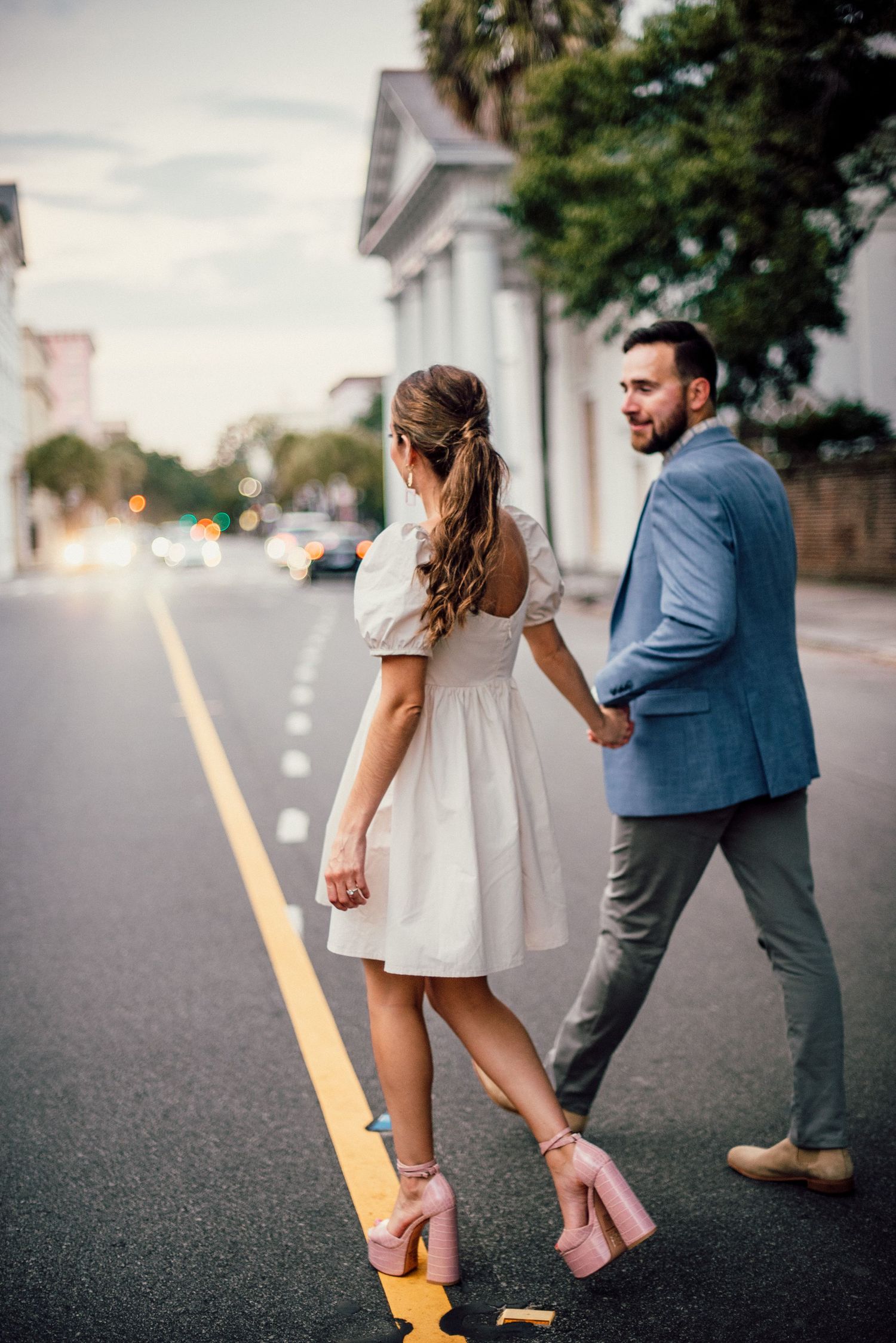 Playful couple walking along yellow street line in formal attire.
