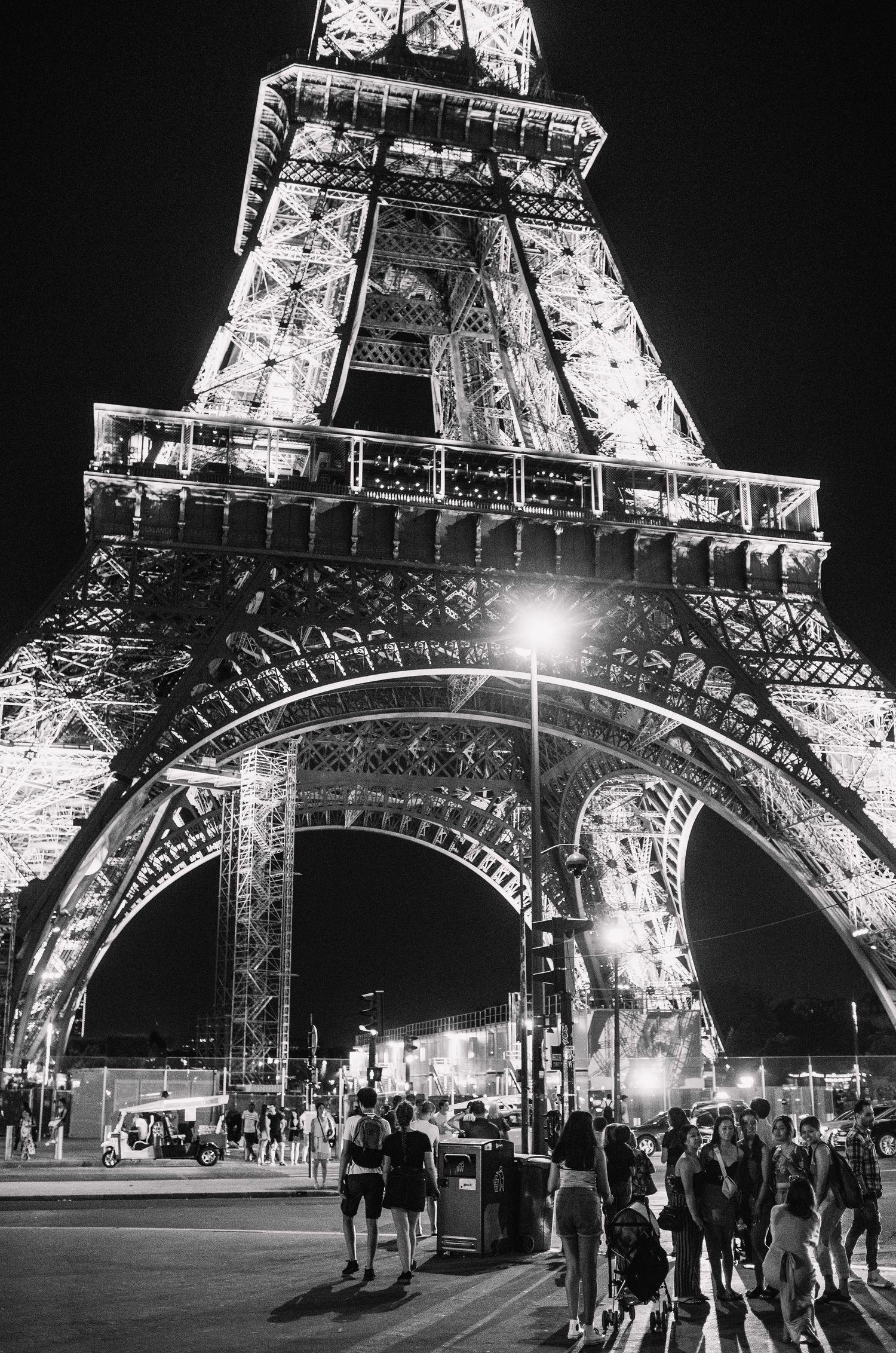 Illuminated Eiffel Tower base at night with tourists gathering underneath in black and white.