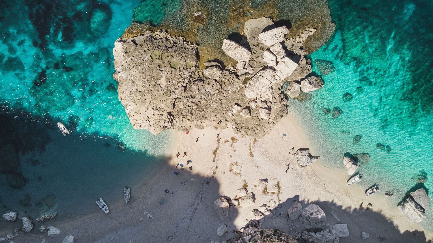 Underwater view of a rocky Mediterranean coastline with vibrant turquoise waters and coral formations.