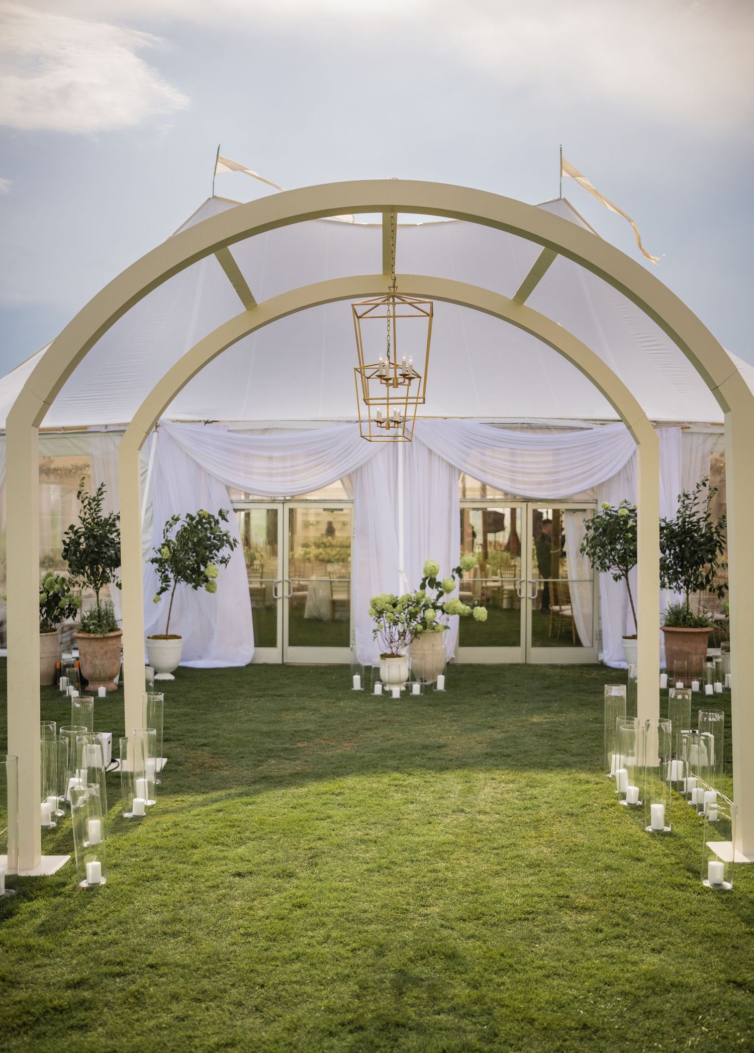White arched walkway decorated with flowing fabric and floral arrangements for an outdoor wedding ceremony.