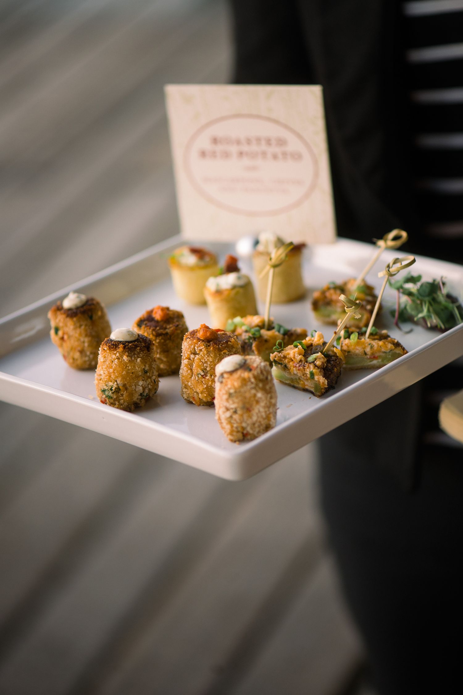 Elegant plated appetizers with garnish served on white rectangular plates in moody lighting.