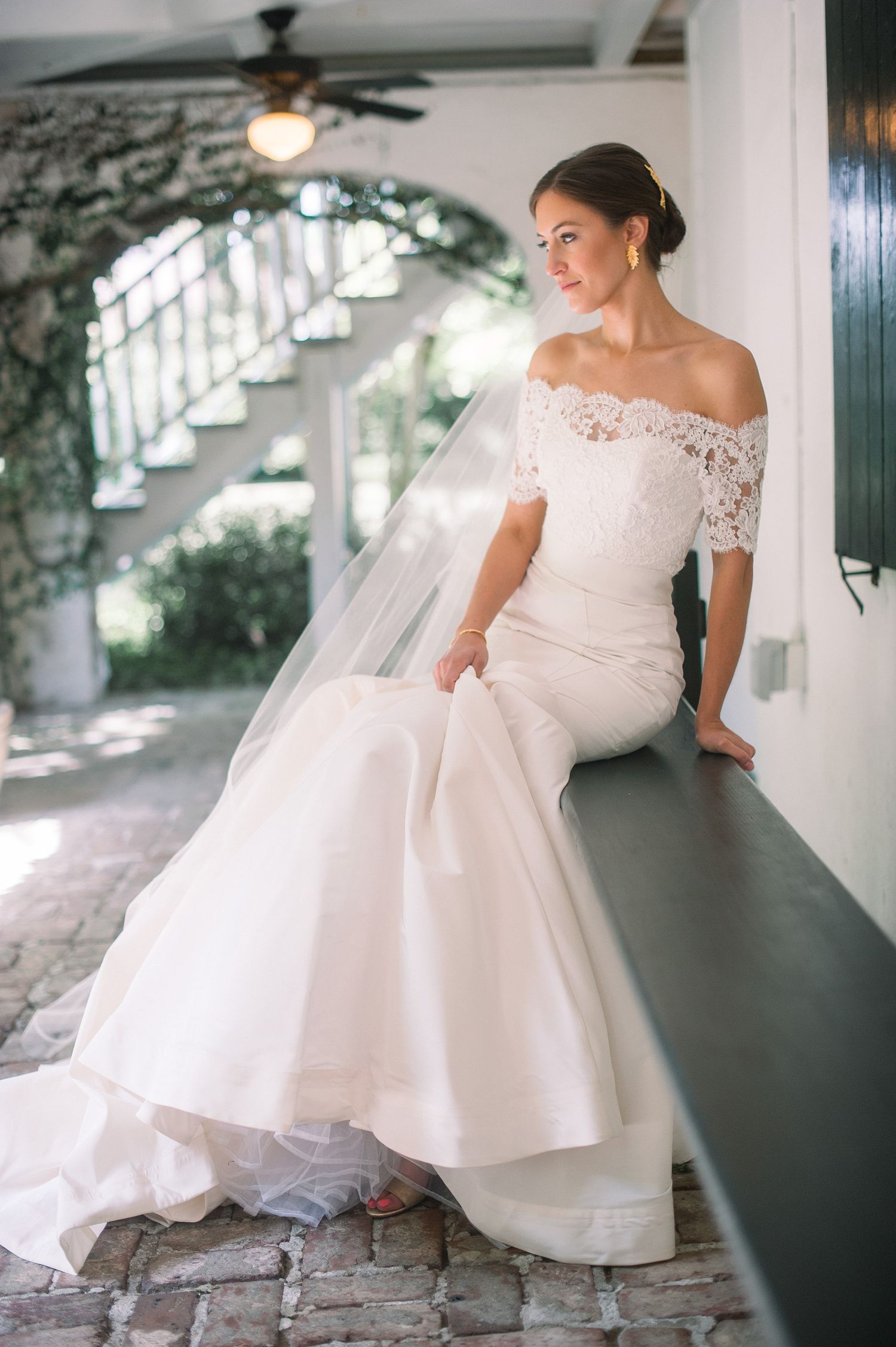 A bride in an elegant off-shoulder lace wedding dress poses gracefully on a staircase in a series of romantic portraits.