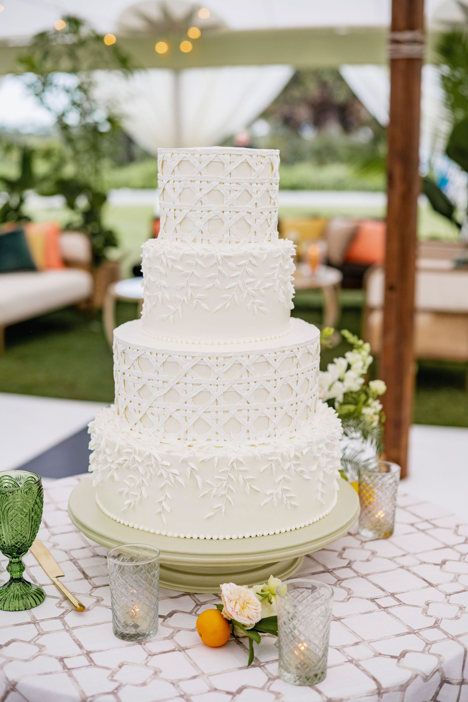 Three-tiered white wedding cake with delicate lace pattern details displayed on a table with floral accents.