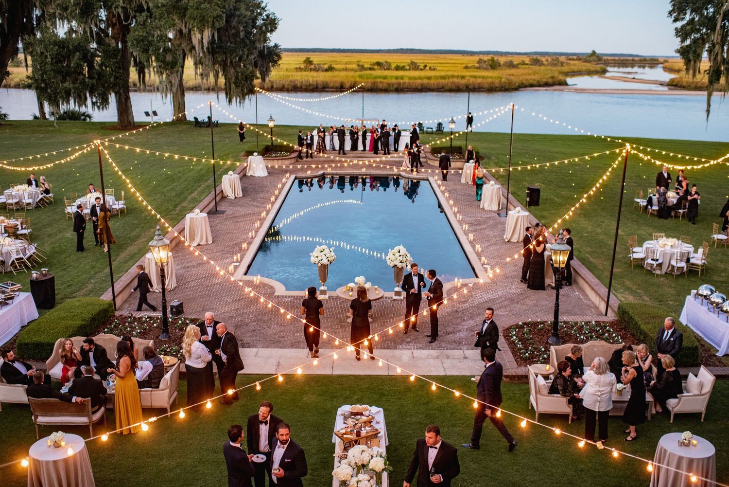 A romantic outdoor wedding ceremony and reception at dusk with string lights illuminating the venue space.