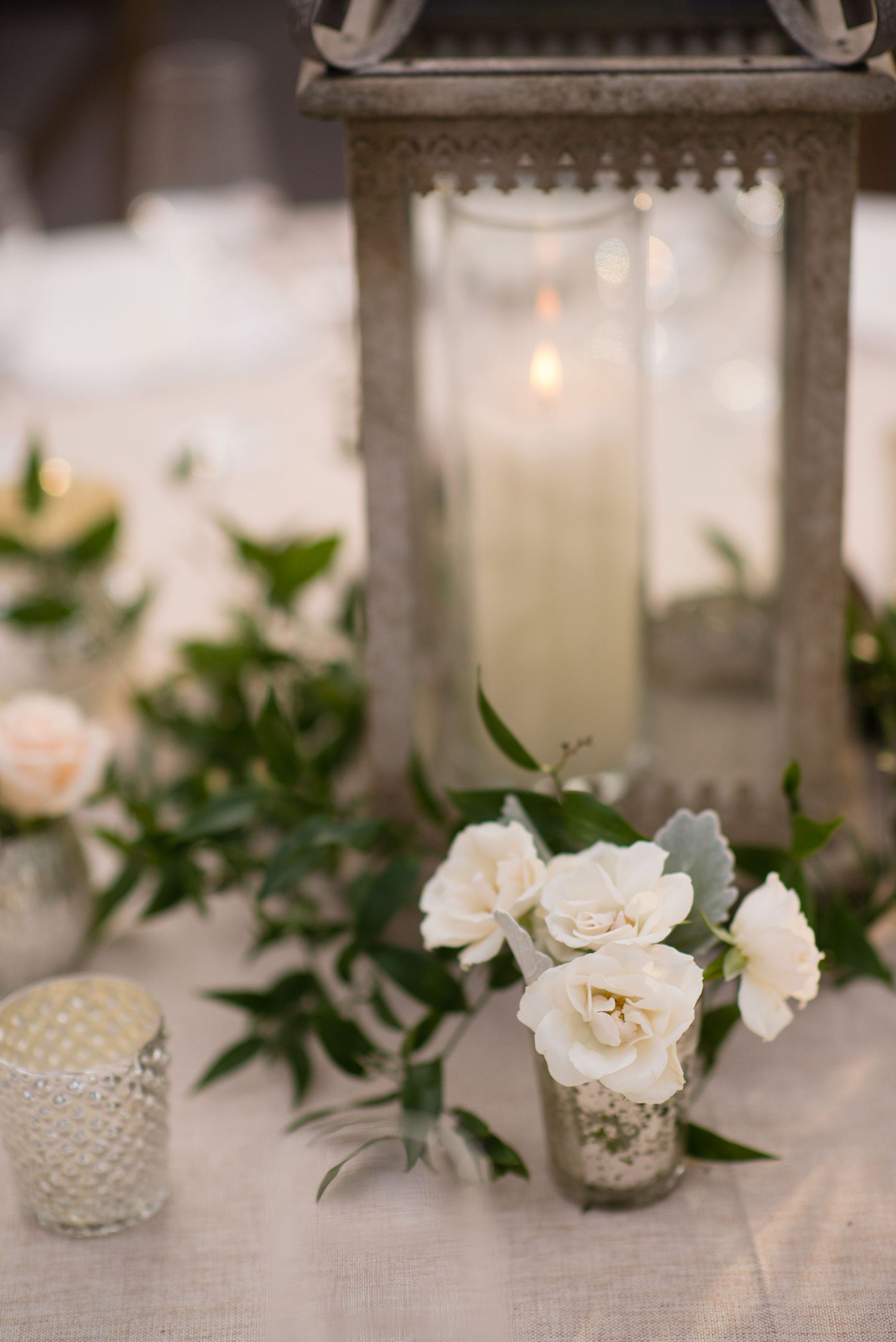 White gardenia flowers and greenery arranged in small glass votives as elegant table centerpieces.