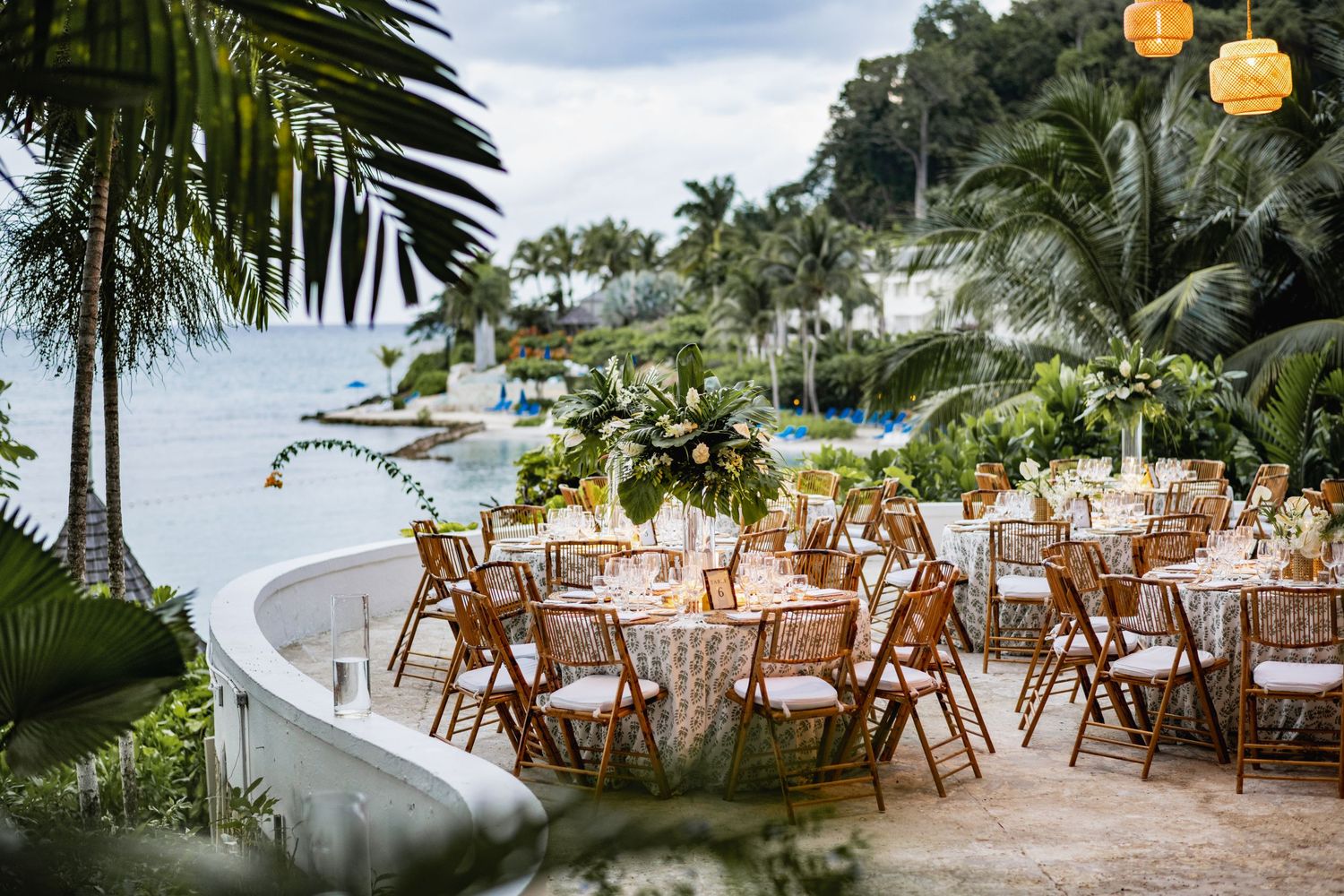 Elegant outdoor beach wedding reception setup with wooden chairs and tables under palm trees at a tropical resort.