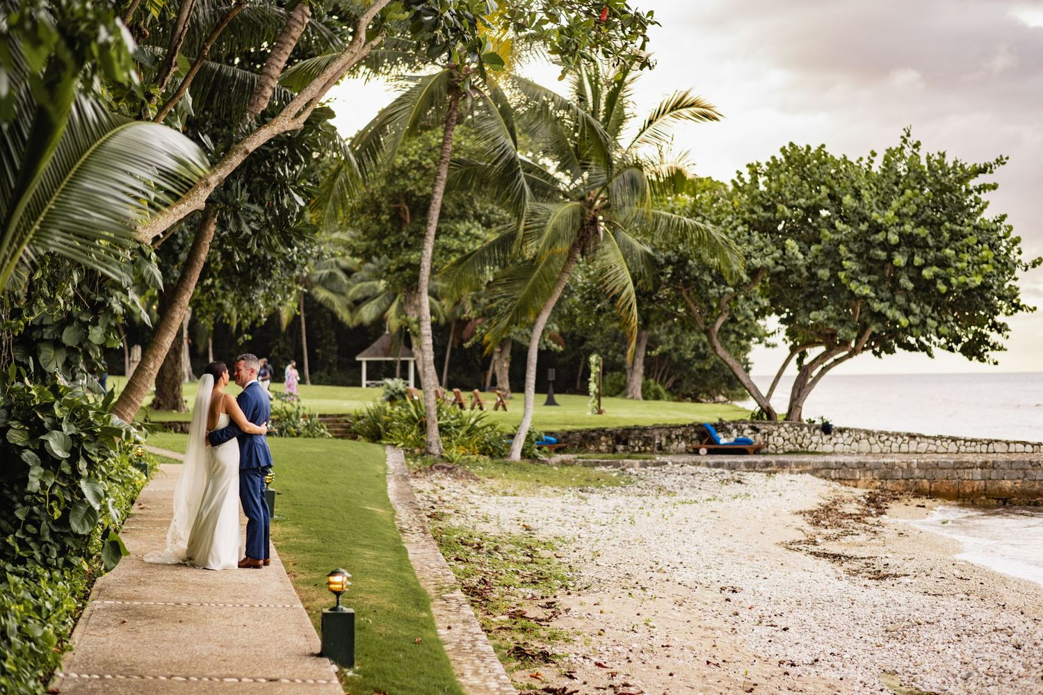 A scenic beach wedding ceremony setup with palm trees, white chairs, and tropical landscaping along the shoreline.