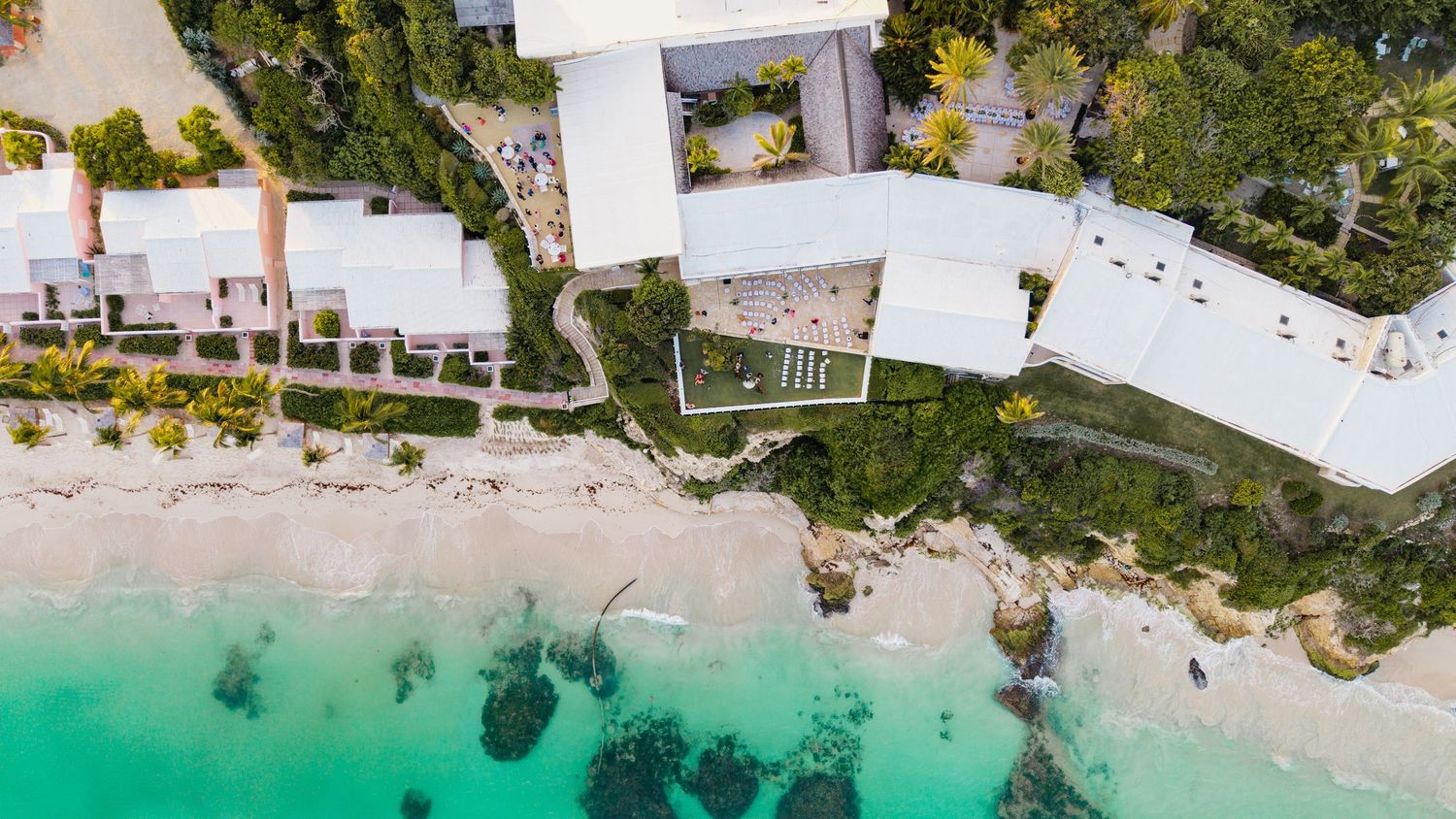 Aerial drone shot of white beach resort buildings along turquoise Caribbean waters.