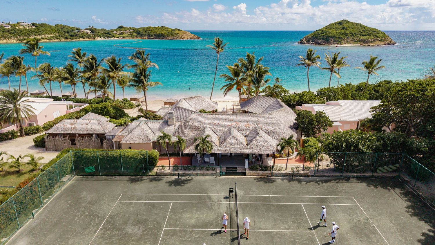 Aerial view of a beachfront resort with palm trees and thatched-roof bungalows.