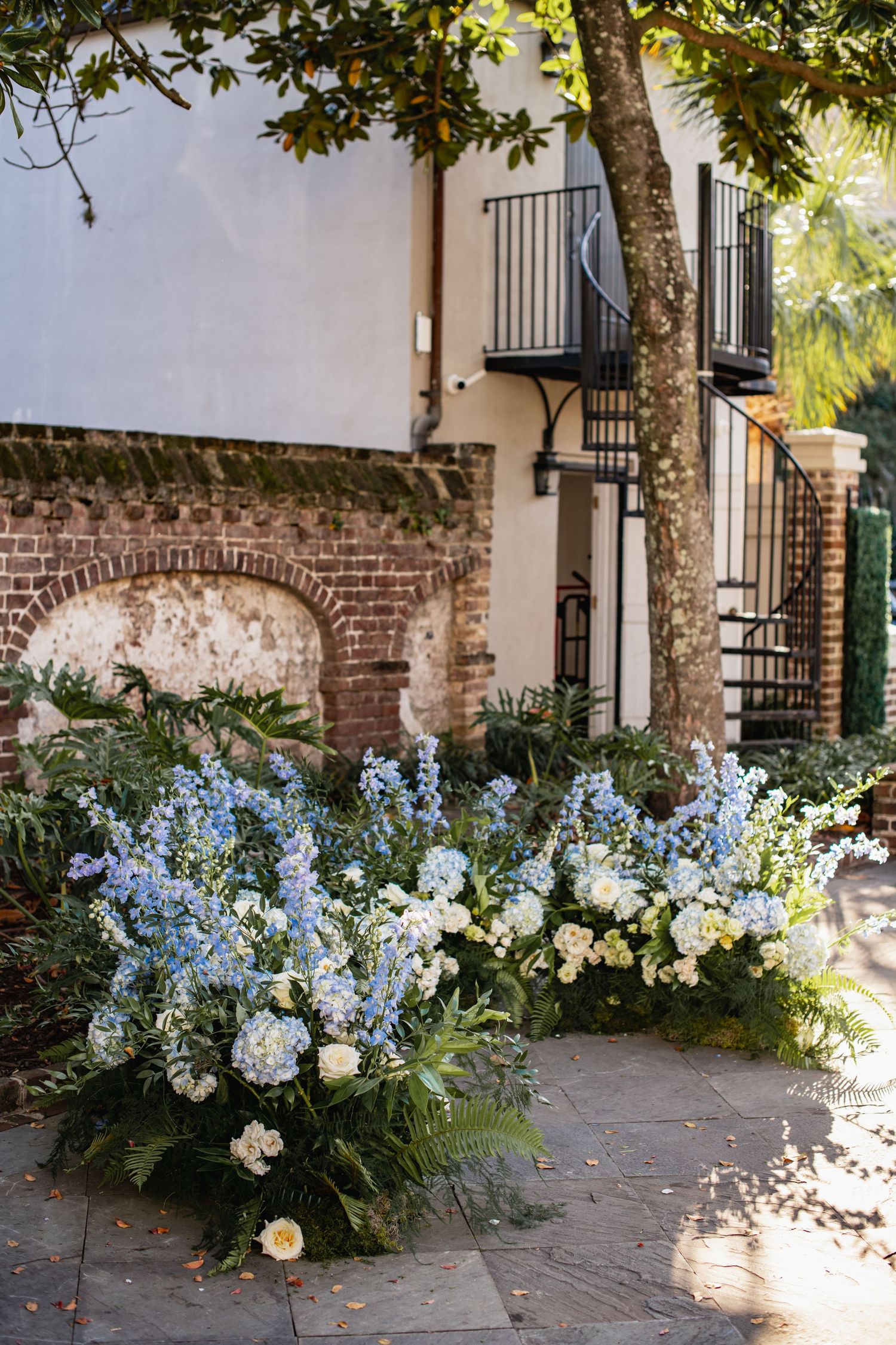 Beautiful blue and white floral arrangements line a brick courtyard wall creating an elegant outdoor garden display.