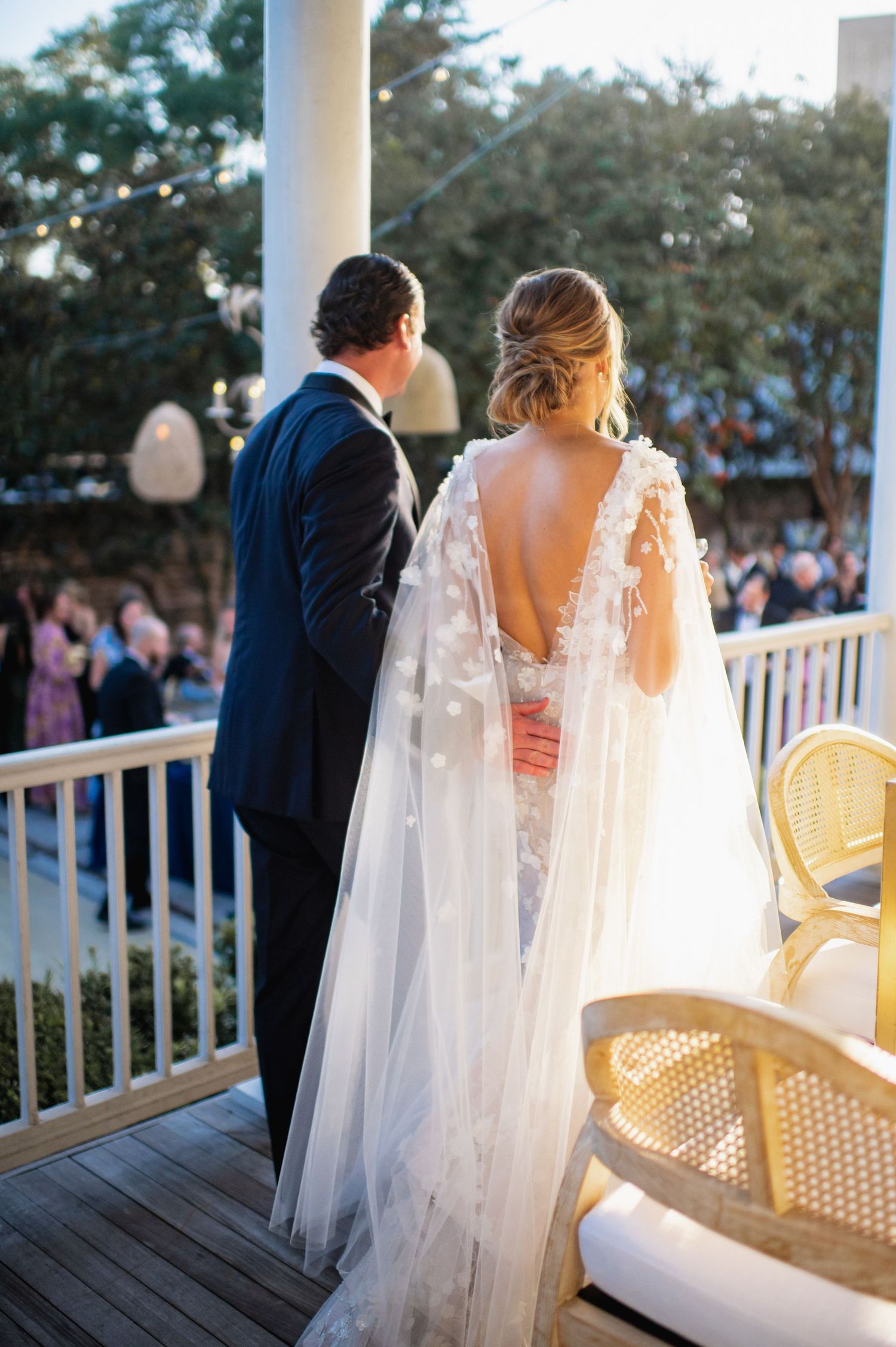 A bride and groom share an intimate moment on a white porch during their outdoor wedding celebration at sunset.