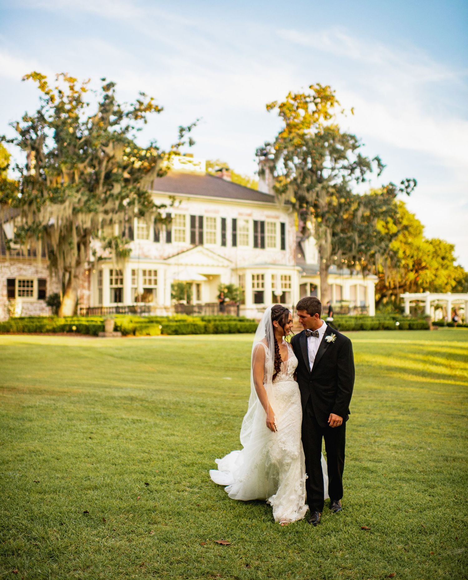 A couple shares a romantic moment on the lawn of a grand southern estate with Spanish moss draped trees.